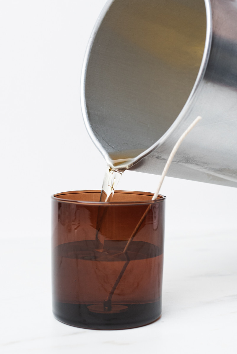 Liquid candle wax pours from an aluminum pitcher into an amber glass straight sided tumbler jar from CandleScience.