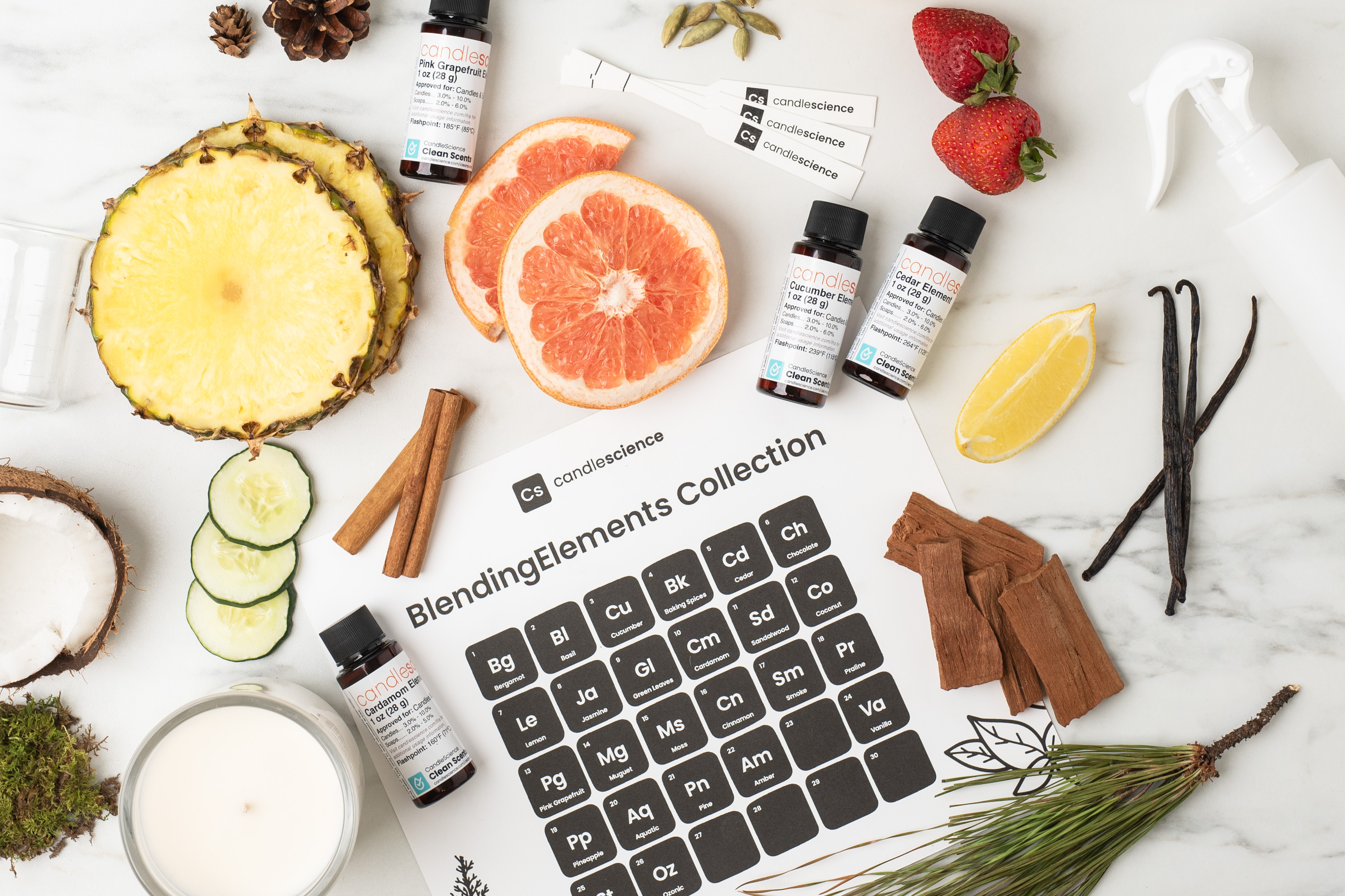 A Periodic Table of BlendingElements chart with 1 oz fragrance bottles, slices of citrus fruit, sandalwood chips, and fragrance blotters are a white marble counter.