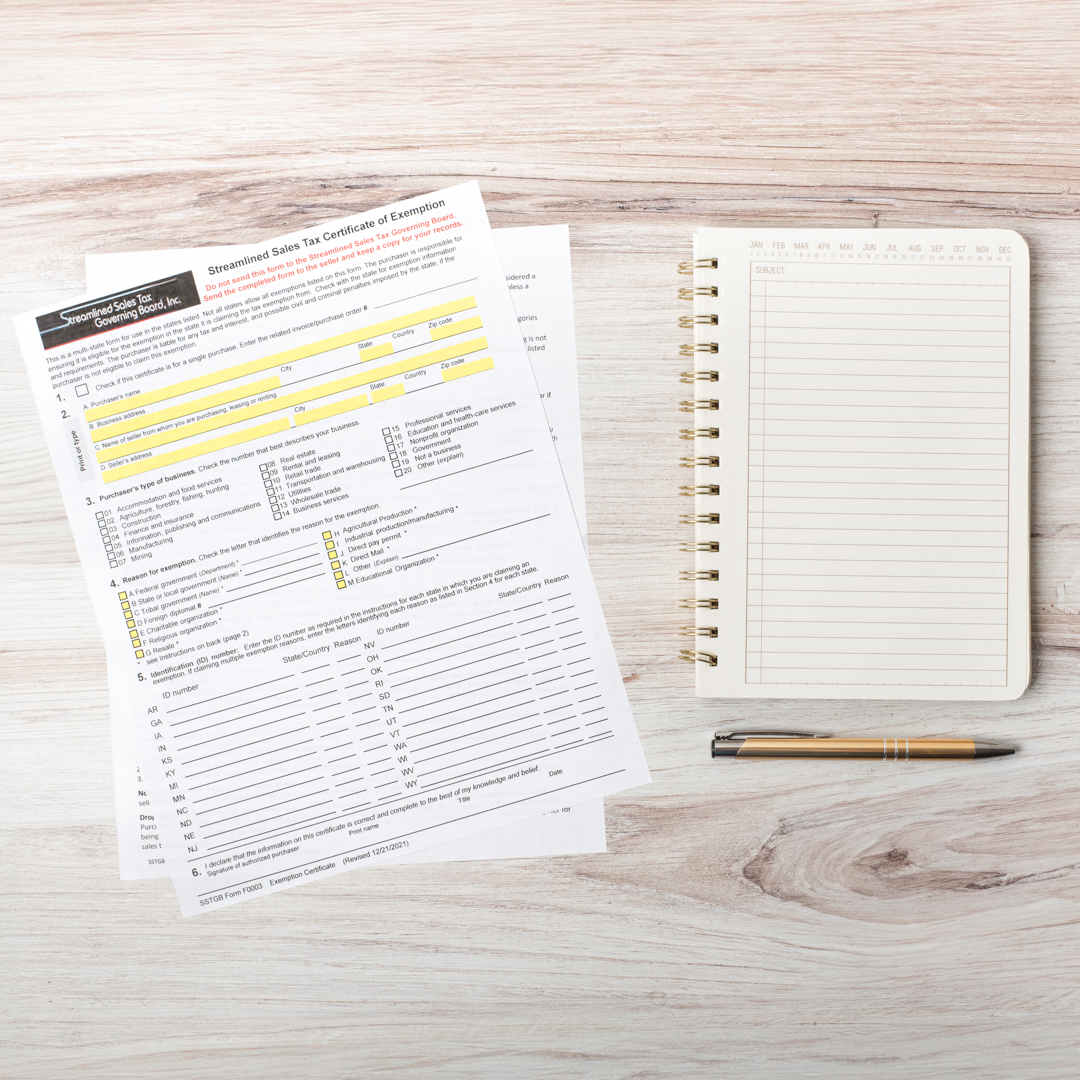 A sales tax exemption form sits on a wooden desk next to a notebook and pen.