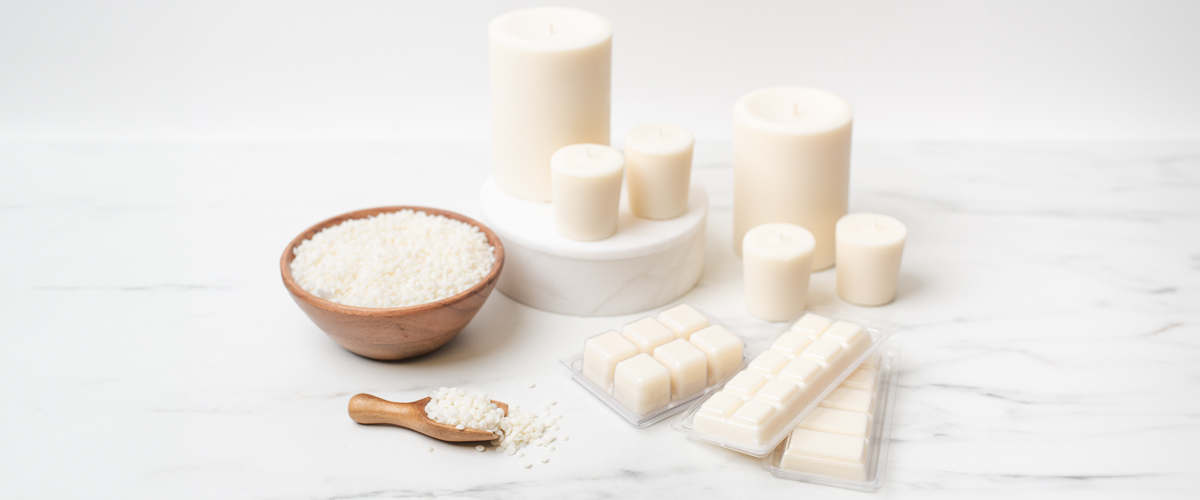 A wooden bowl of pastillized CandleScience CocoSol Soy Pillar Wax with several pillars and wax melts staged on a marble tabletop.