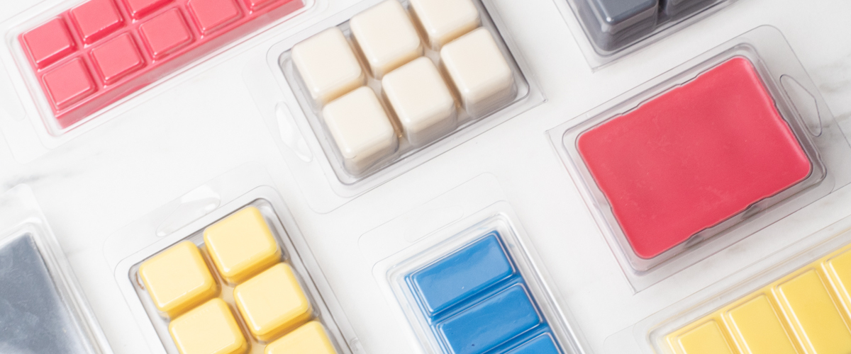 A variety of red, white, yellow, and blue wax melts in 6 piece clamshells on a white countertop.