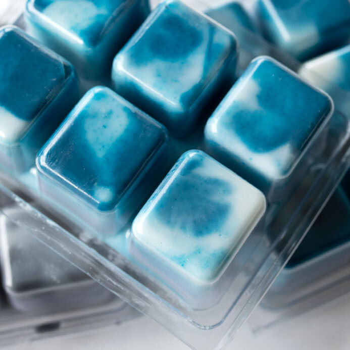 White wax melts with blue swirls in a clear, plastic clamshell