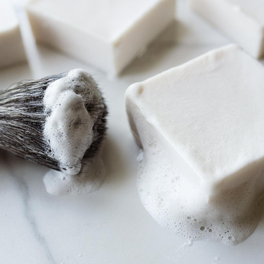 A lathered handmade shave bar next to a shaving brush