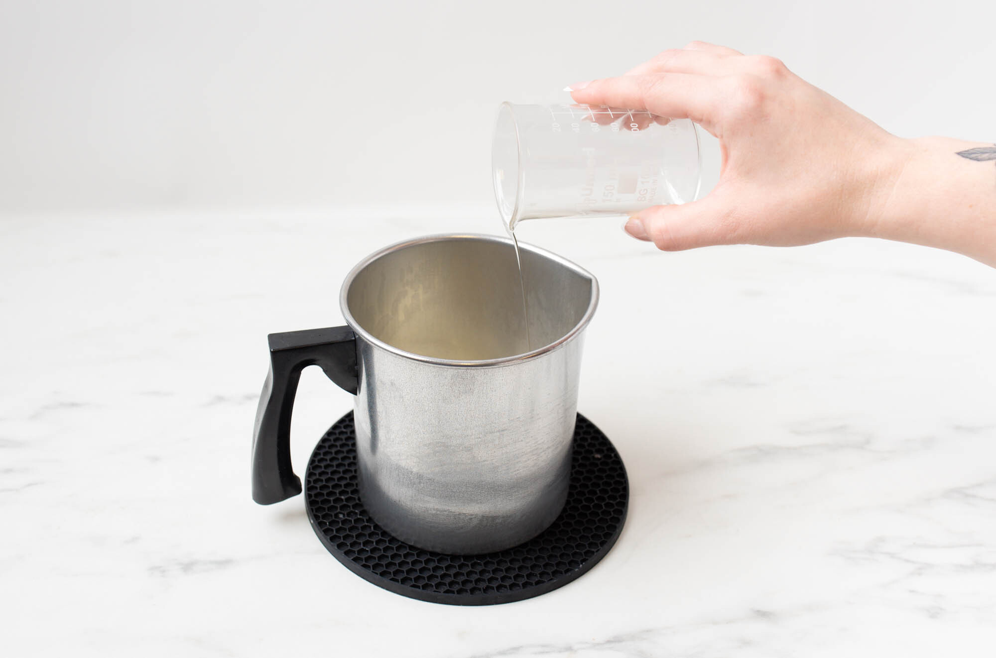 Adding fragrance oil to melted wax in a pouring pitcher.