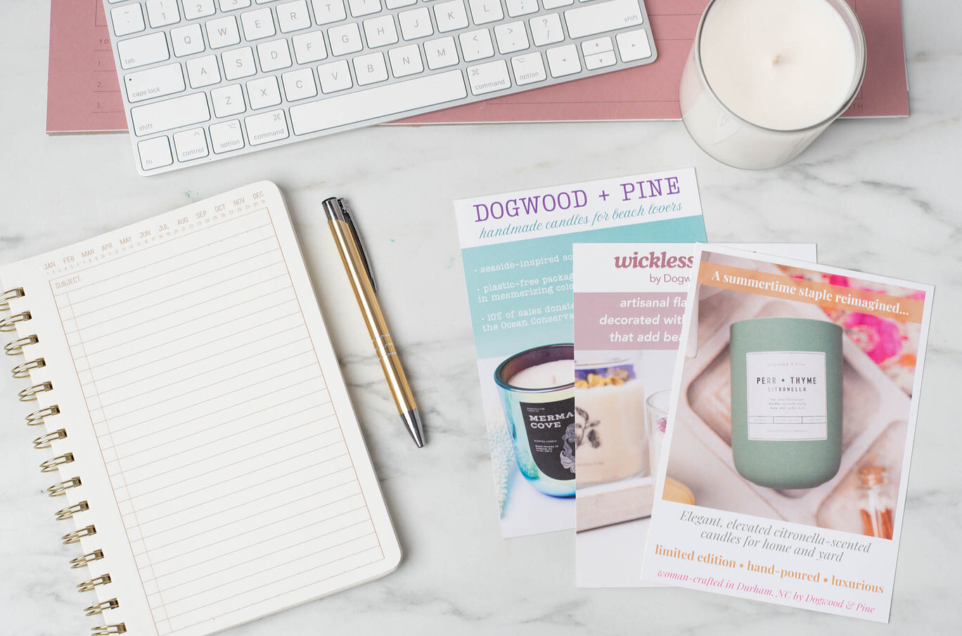 Three shelf talker postcards promoting Dogwood + Pine Candle Co. products spread across a desk 