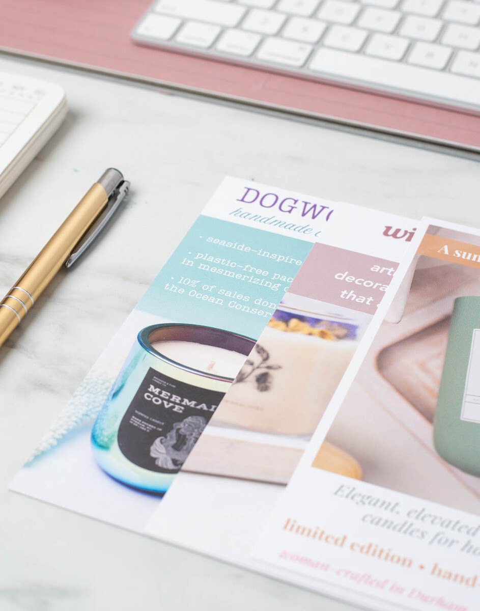 A close-up of three shelf talker postcards promoting Dogwood + Pine Candle Co. products on a desk 