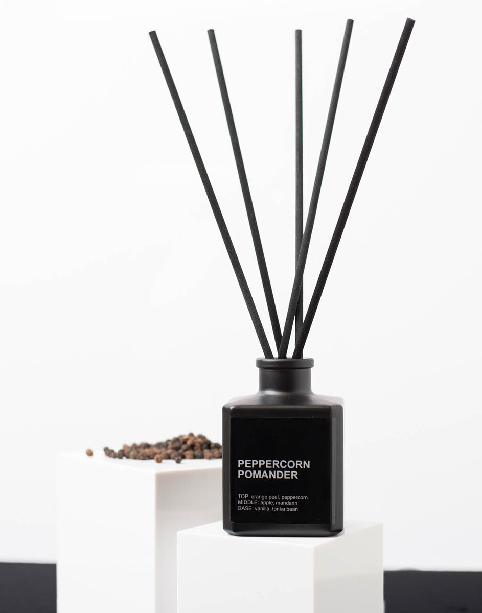 A matte black reed diffuser bottle with black reed diffuser sticks sits atop a white cube riser.