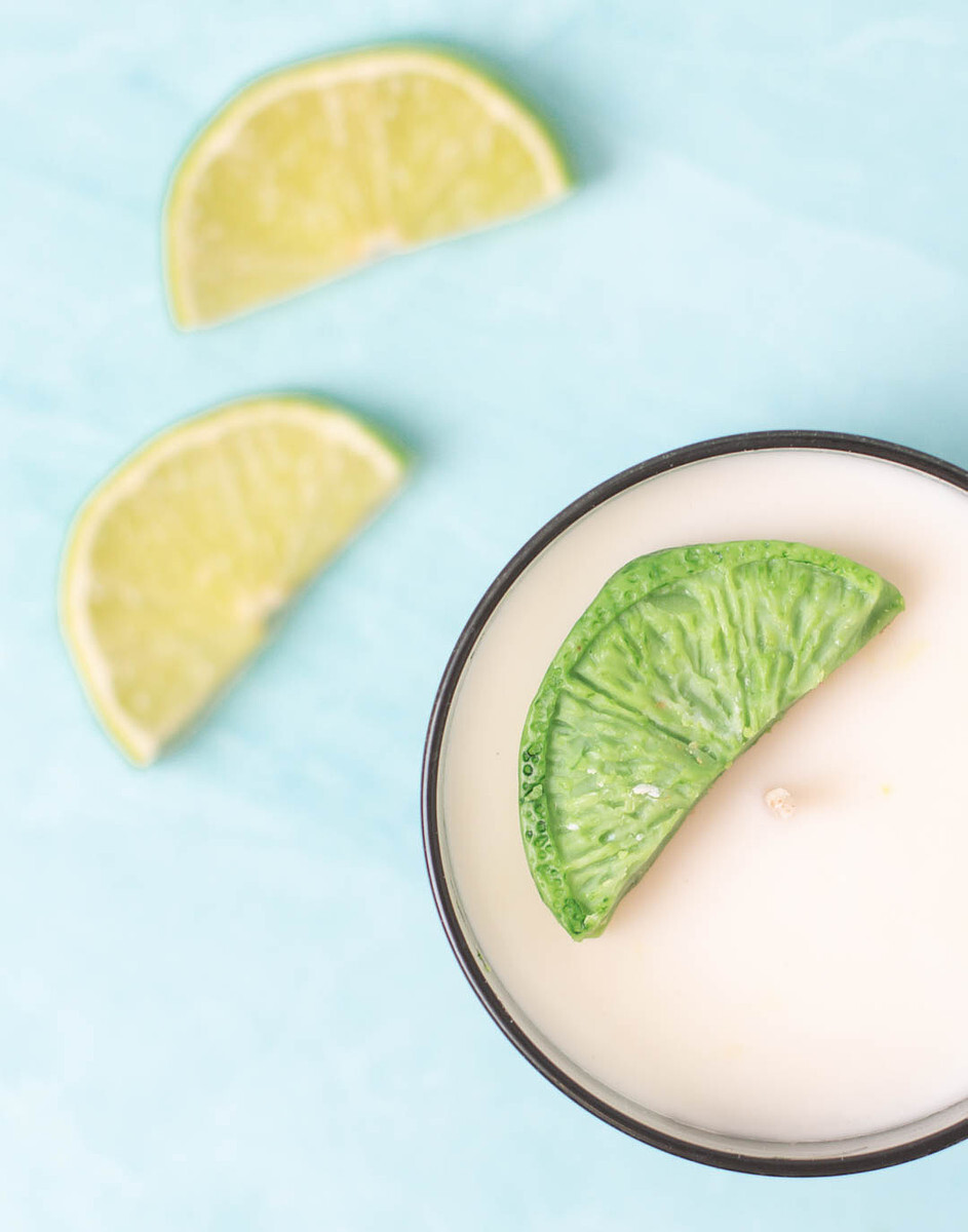 An overhead view of a white handmade candle with a green, lime slice-shaped wax embed.