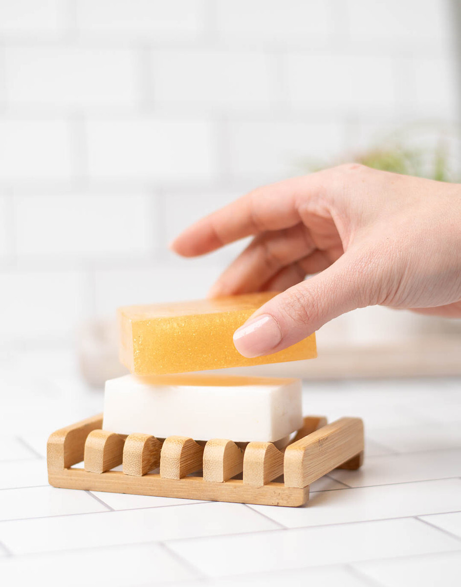 A light-skinned hand holds a bar of shimmery gold, mica-colored melt and pour soap.