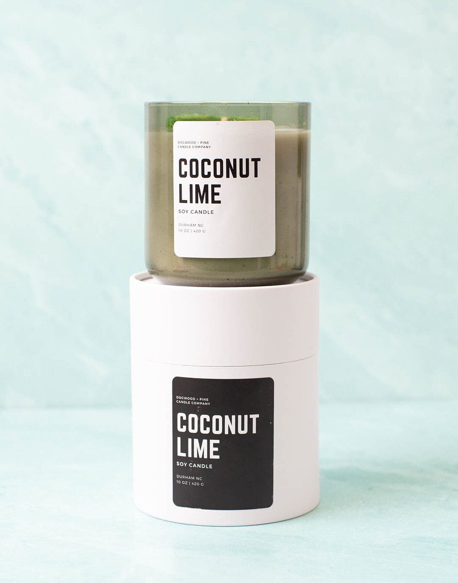 A candle poured in a Smoked Olive Bubble Tumbler Jar sits atop a White Paper Candle Tube with a black label.