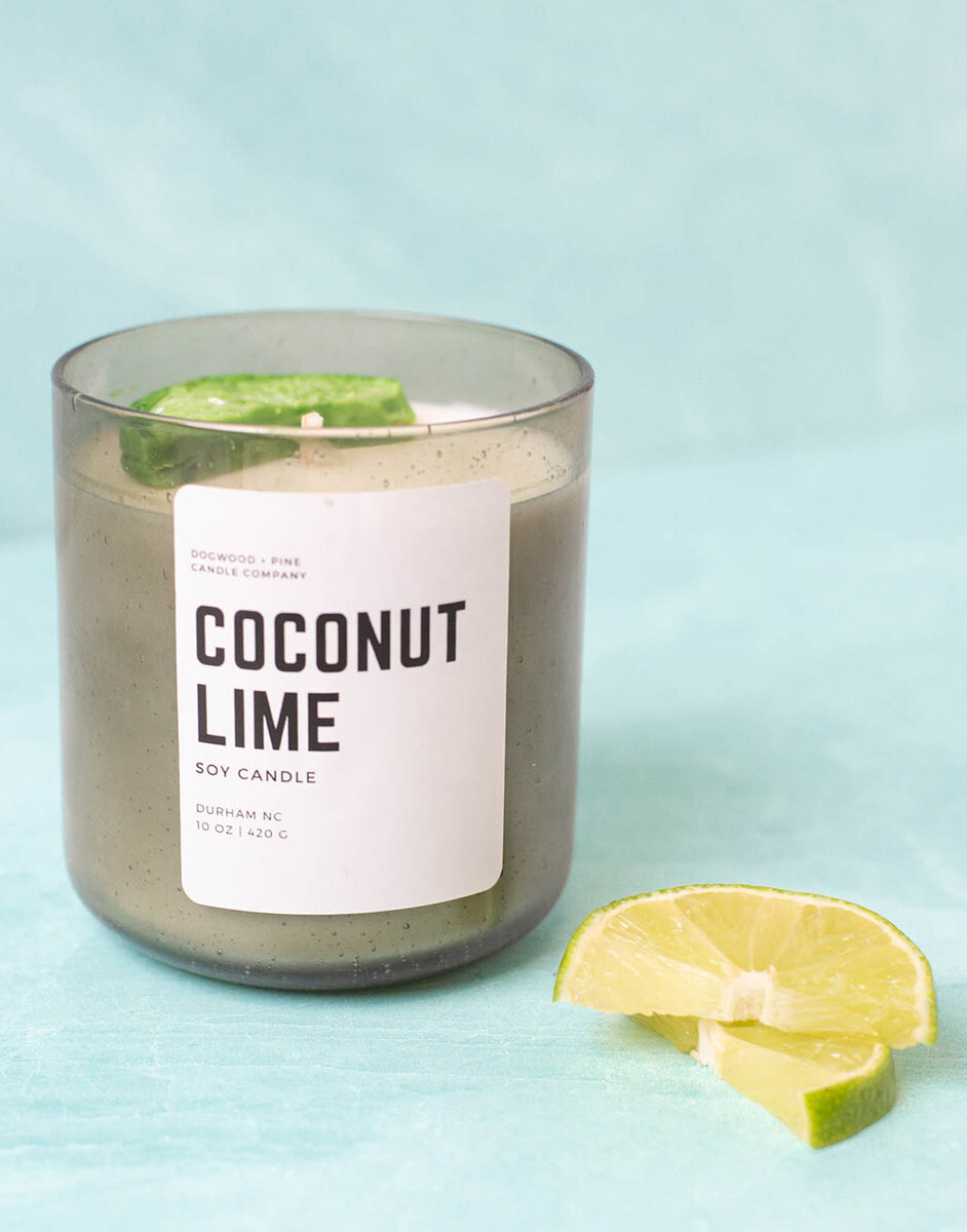 A handmade candle in a Smoked Olive Bubble Tumbler Jar sits next to lime slices.