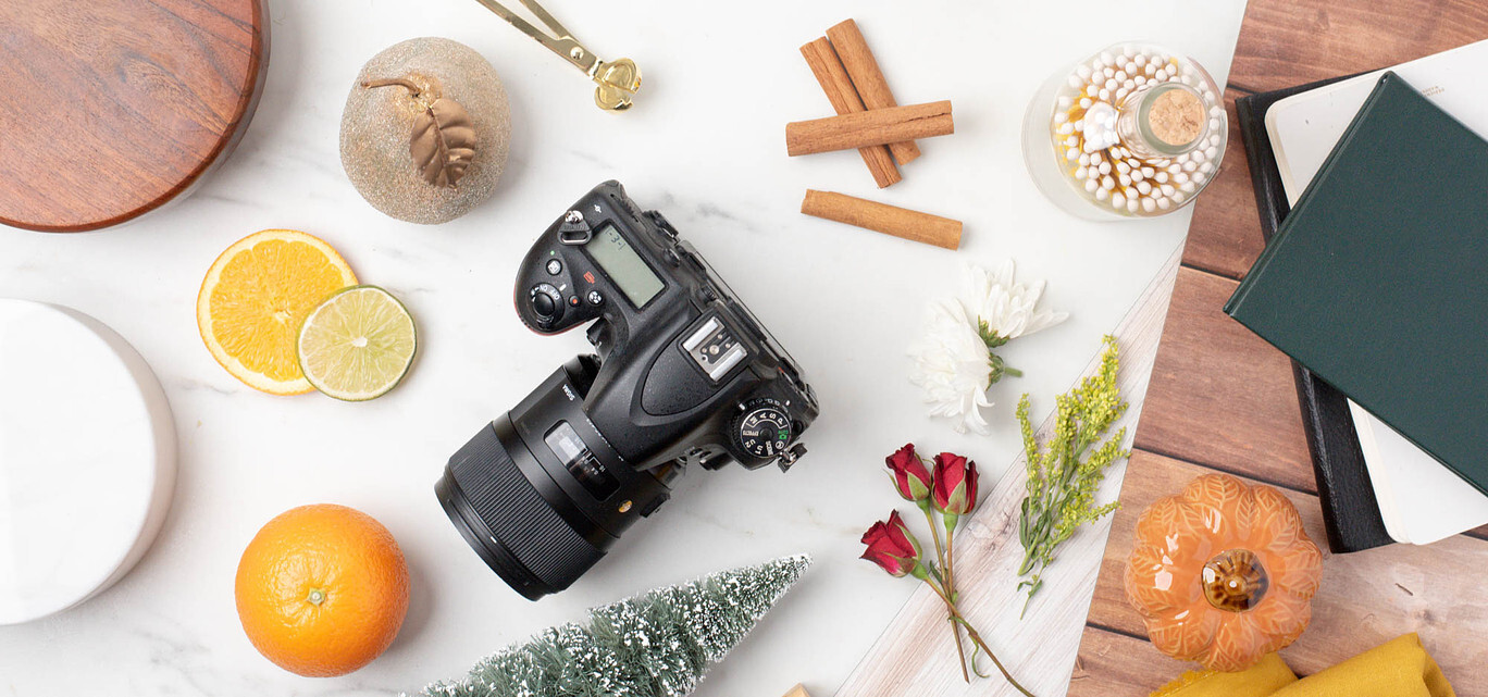 A DSLR camera lays on a tabletop next to a variety of product photography props