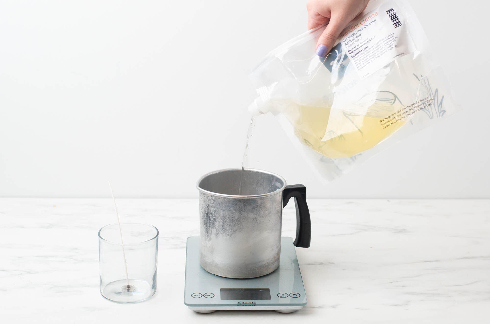 Pouring melted wax from bag into a pouring pitcher on a digital scale.