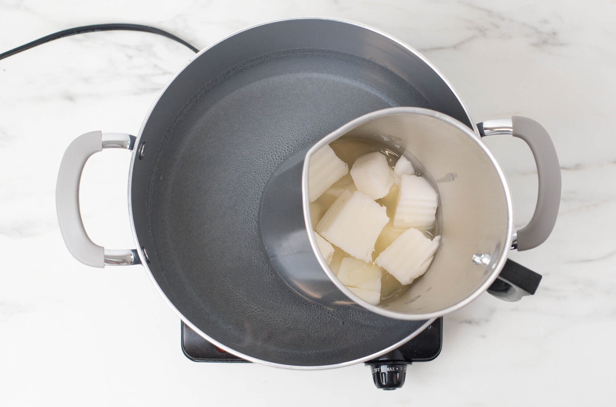 Candle wax melting in a pouring pitcher in a double boiler.