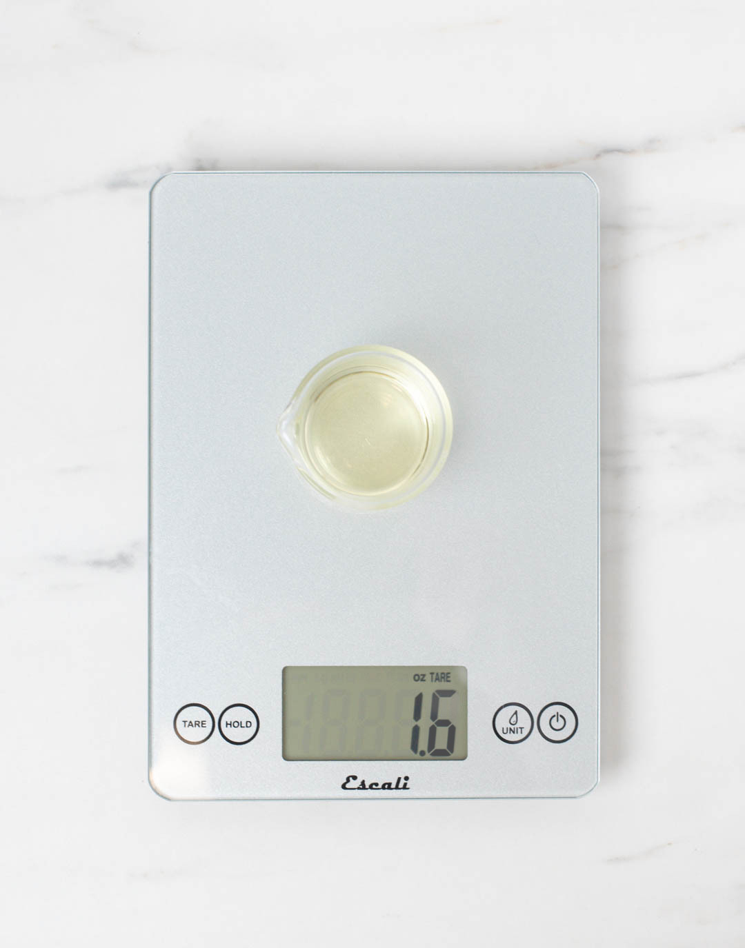 Fragrance oil in a glass measuring cup on a scale weighing 1.6 ounces.