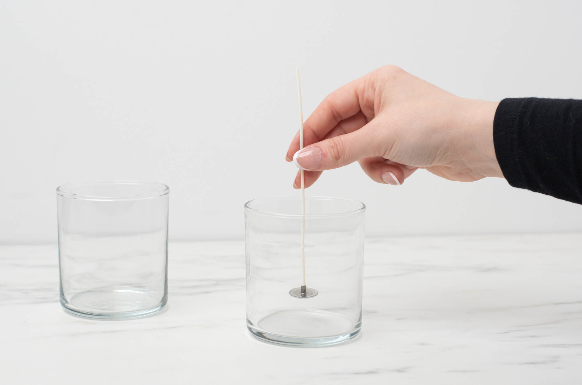 A hand placing a wick into the center of a glass candle jar.