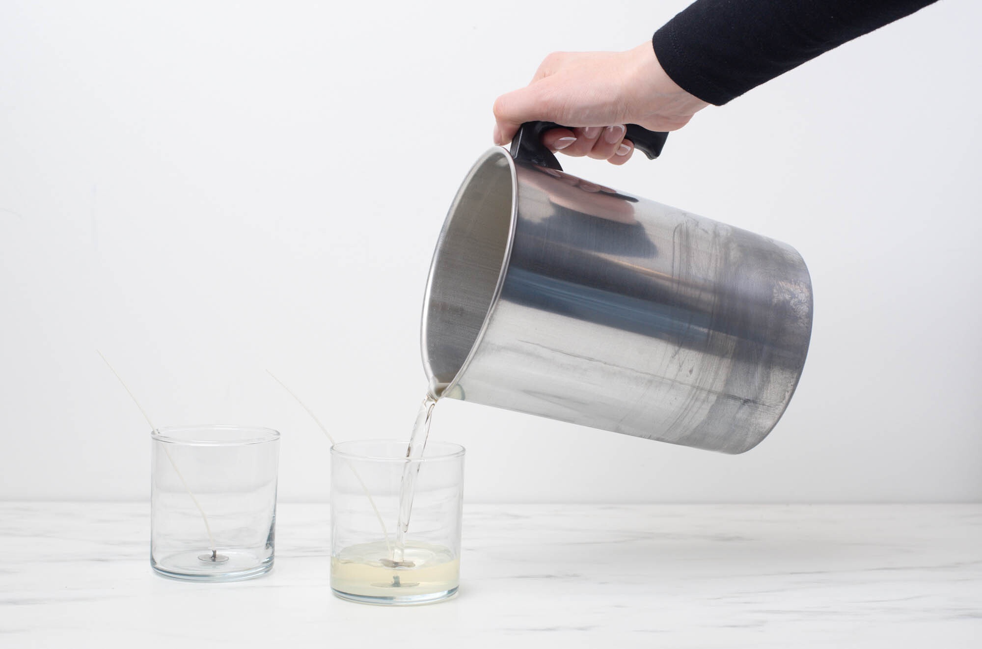 A hand pouring wax into a glass candle jar.