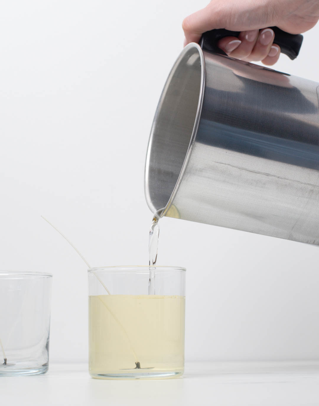 A hand pouring wax into a glass candle jar.