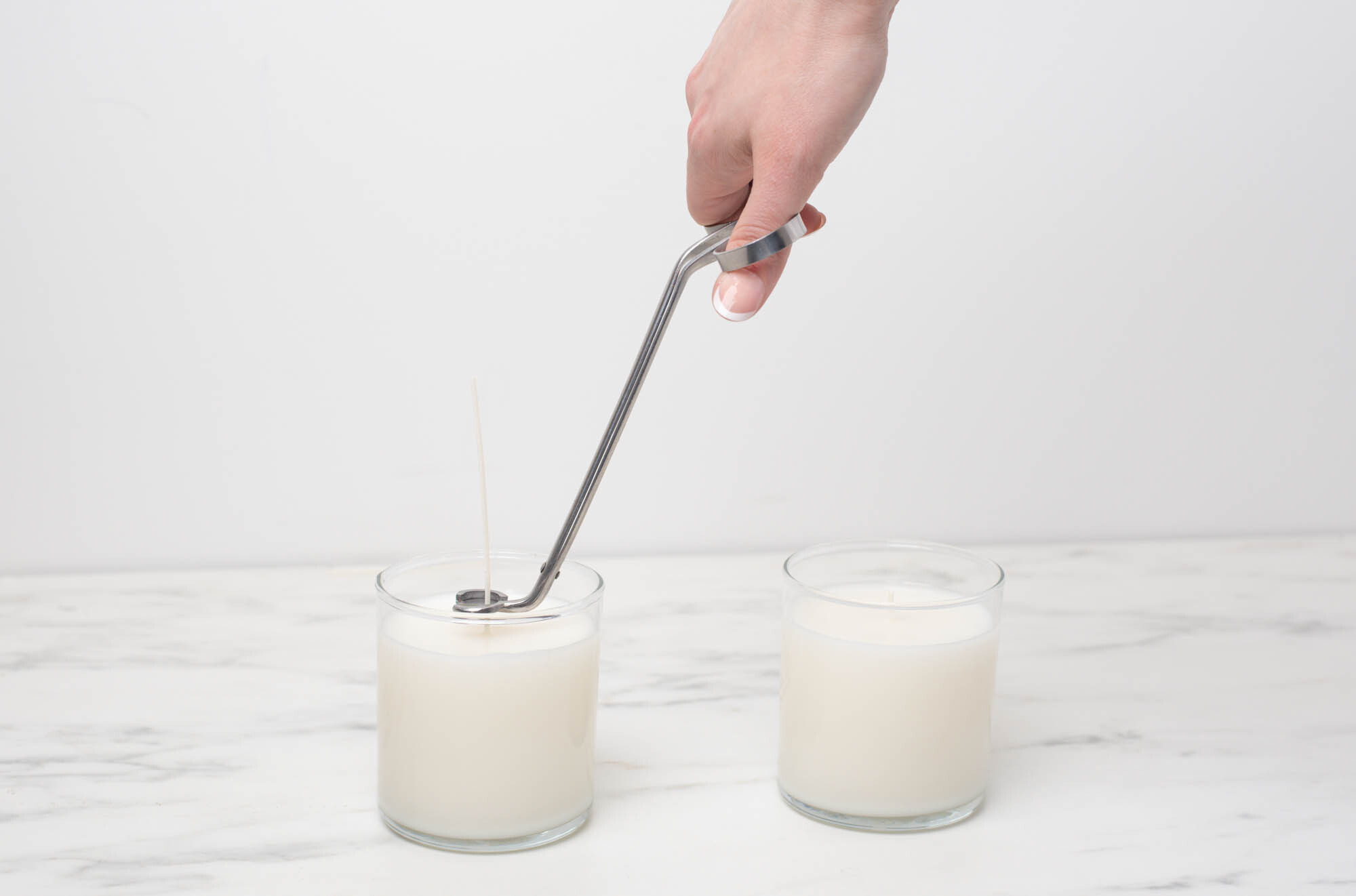 A hand cutting the wicks of candles with wick trimmers.