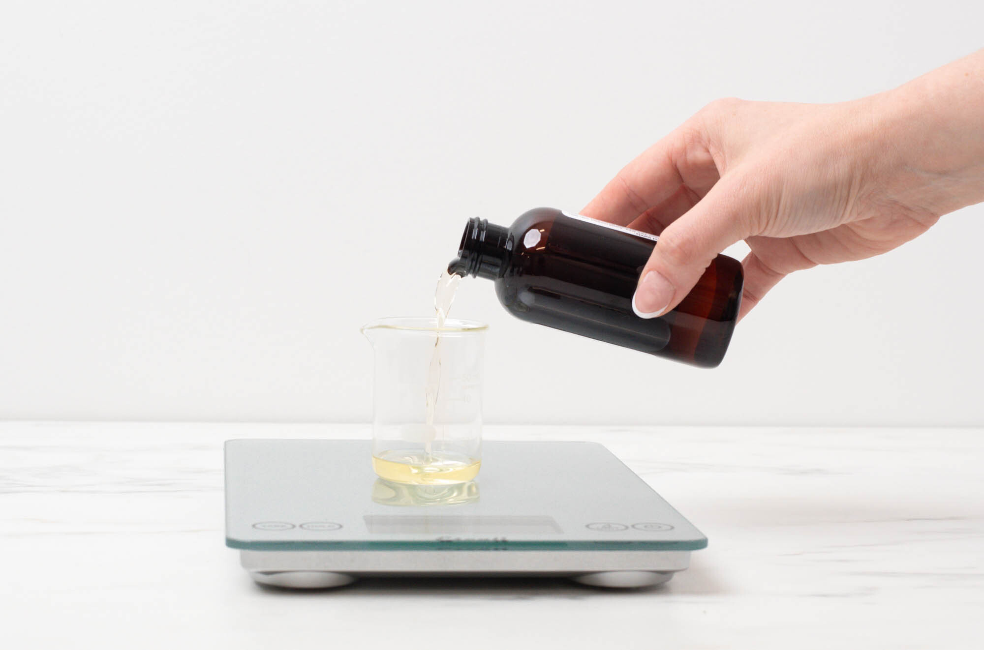 Pouring fragrance oil into a glass beaker on a scale.