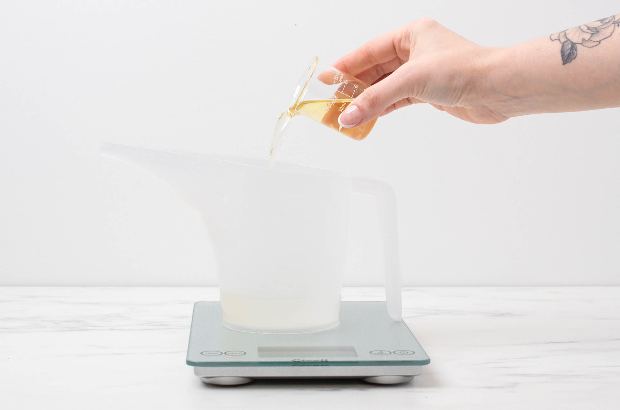 Pouring fragrance into a pouring pitcher with diffuser base in it on a scale.