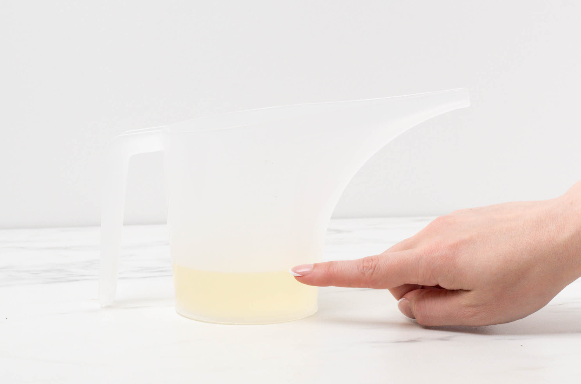 Finger pointing to fluid ounce measurement of mixture in a pouring pitcher.