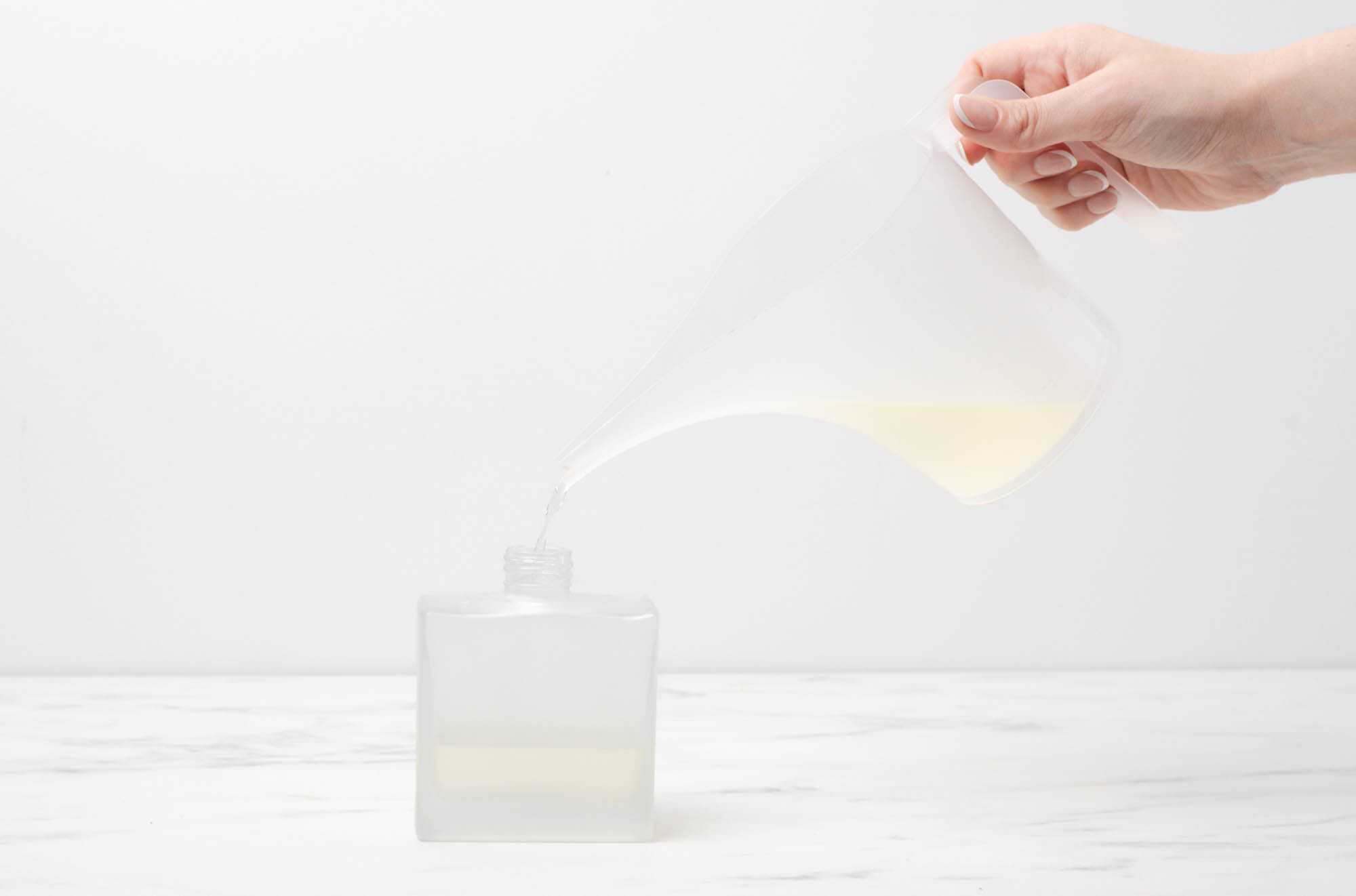 Pouring mixture from pouring pitcher into reed diffuser bottle.