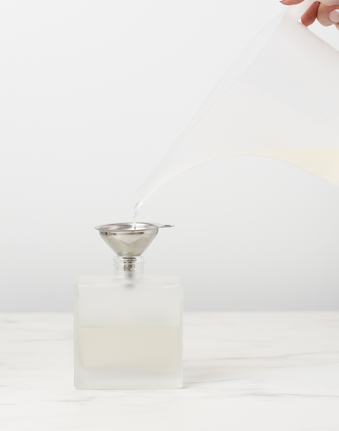 Pouring mixture into diffuser bottle using a silver funnel.