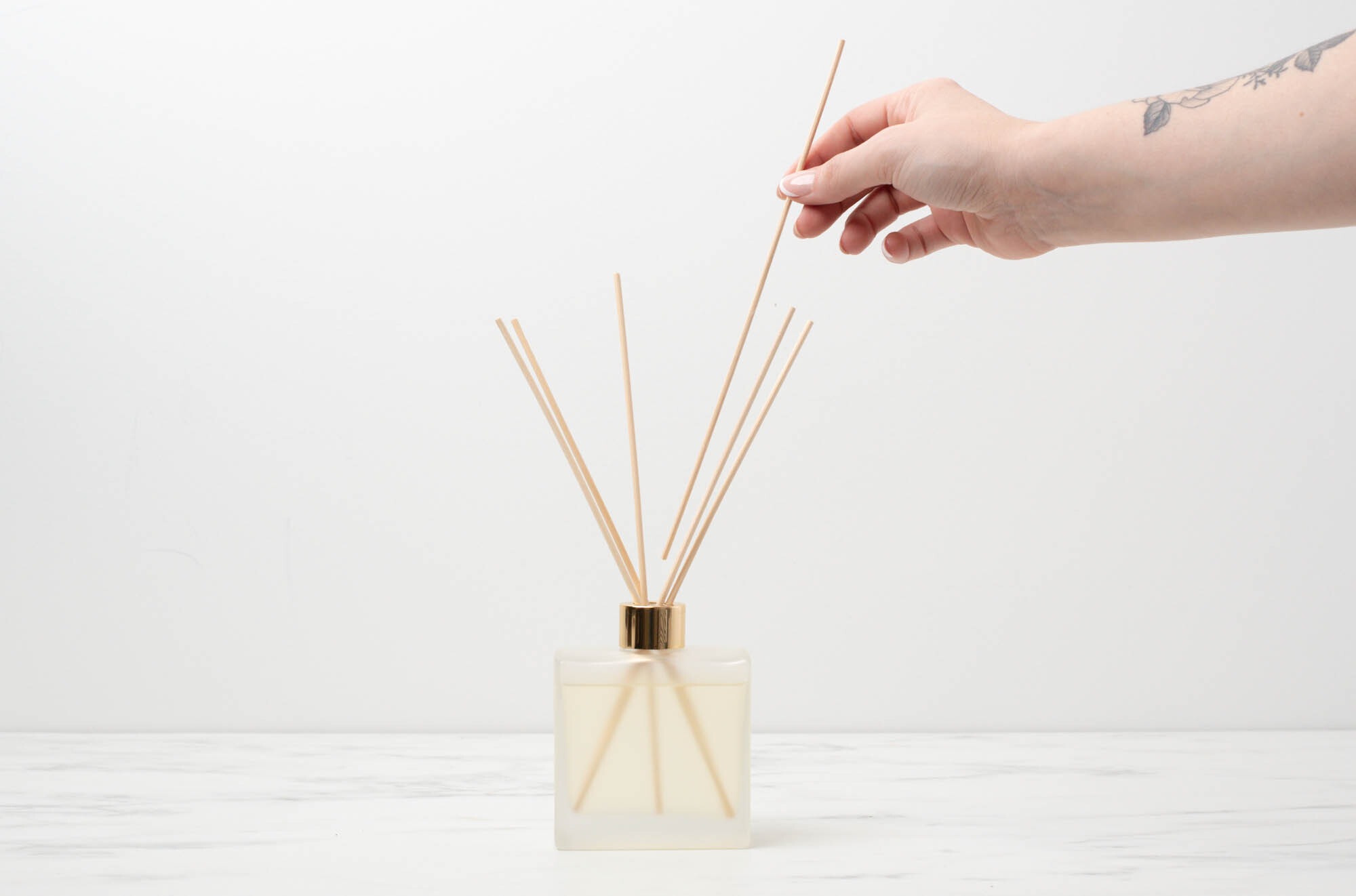 Hand placing 6 reeds into diffuser bottle with gold collar.