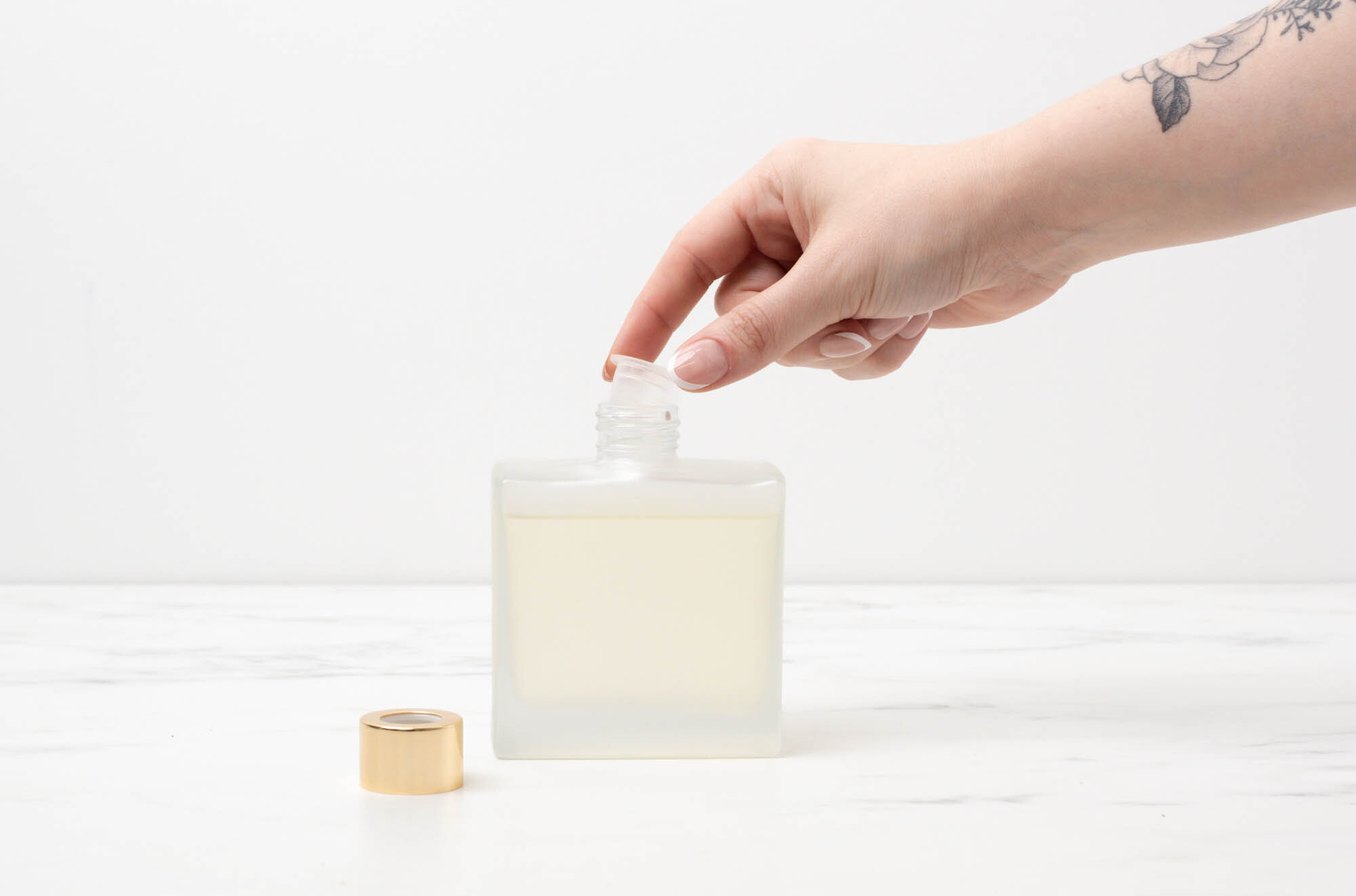 Hand placing clear stopper into neck of reed diffuser bottle.