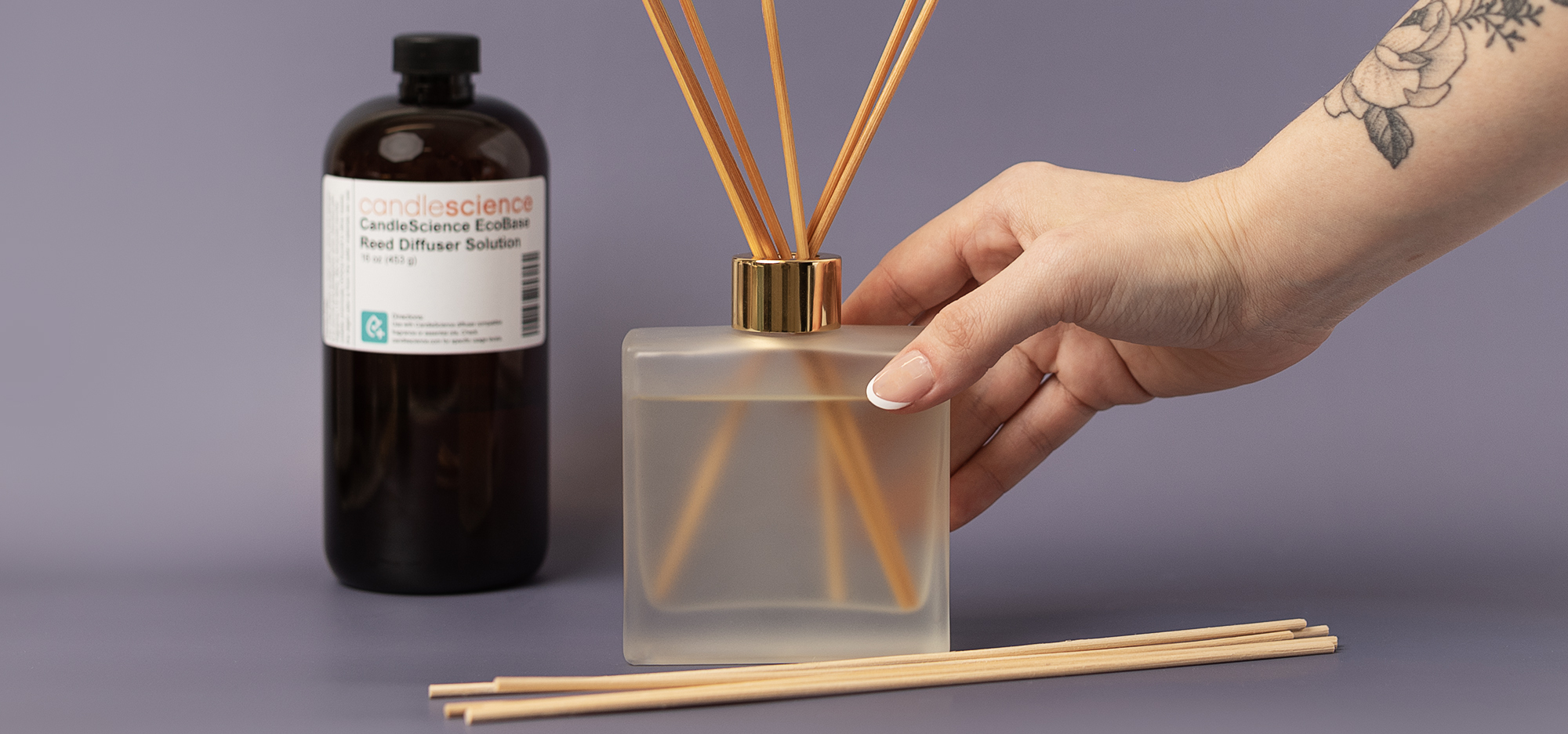 A hand making a reed diffuser using reed diffuser base, fragrance, reeds, and diffuser bottle