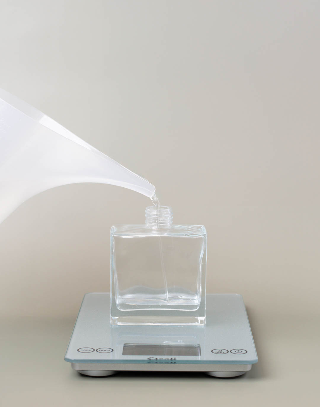 A funnel pouring pitcher filling a glass reed diffuser bottle on a scale. 