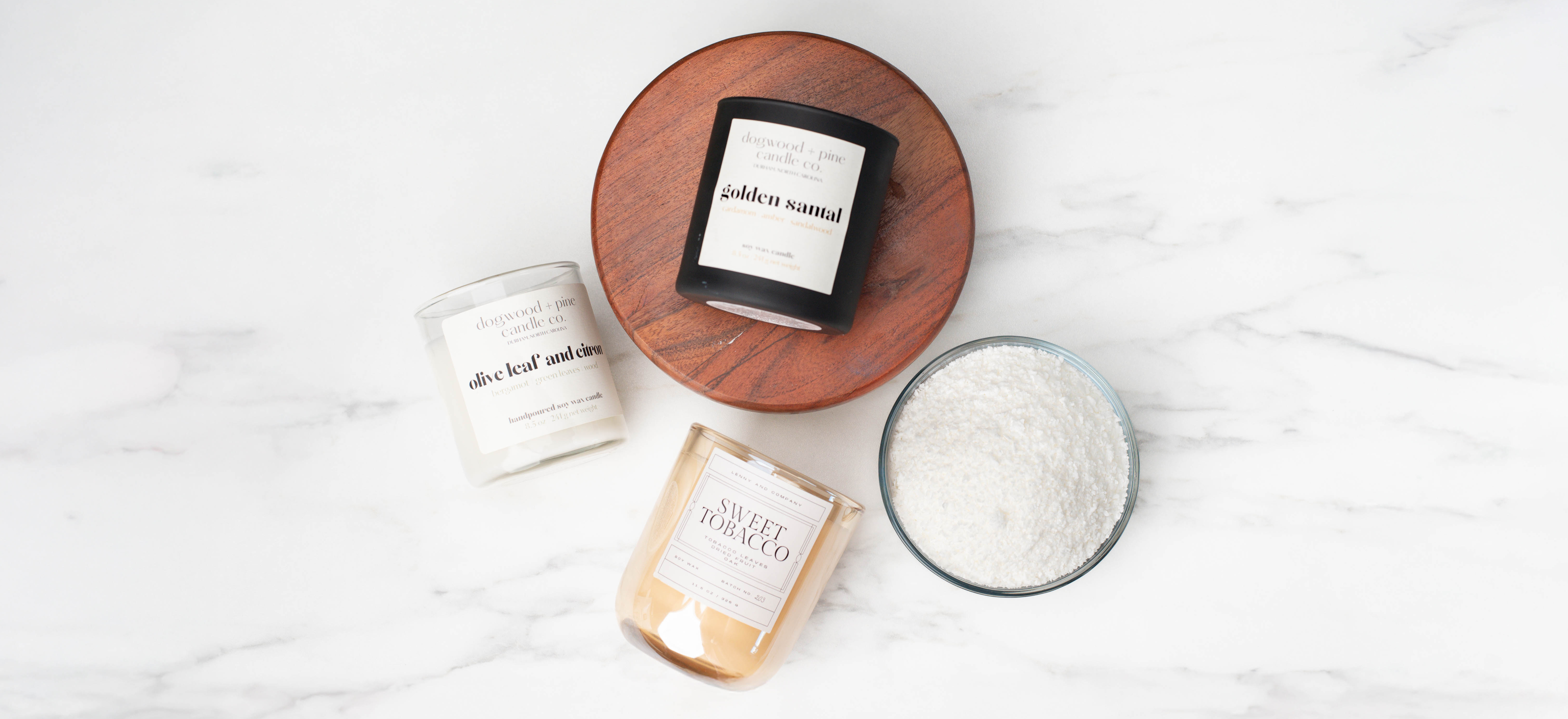 A tumbler, a matte black tumbler jar, and an amber tumbler jar with luxury labels on a bed of ivy with a bowl of CandleScience SimplySoy Artisan wax in a bowl.