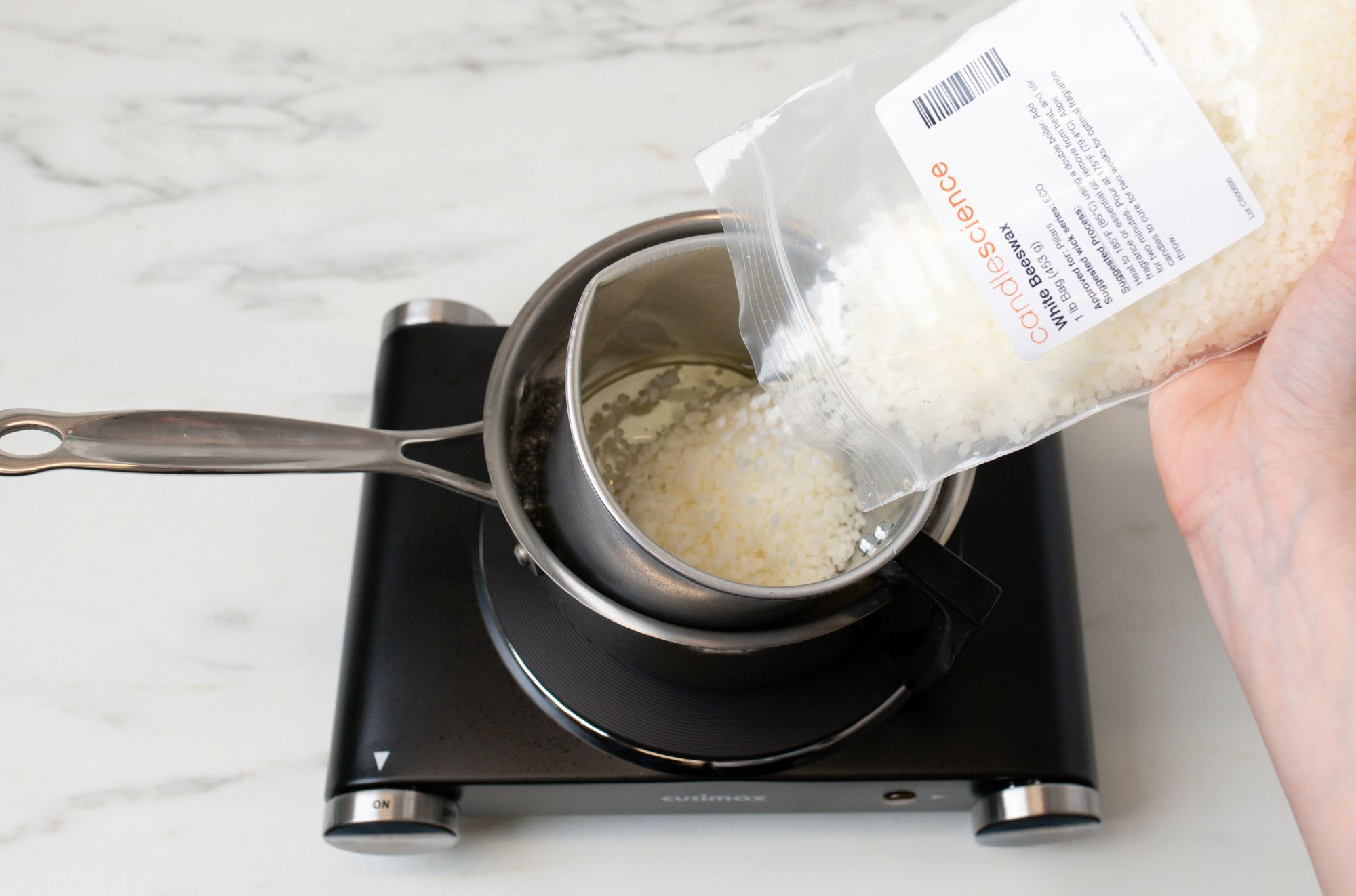 Pouring white beeswax pastilles into a pouring pitcher.