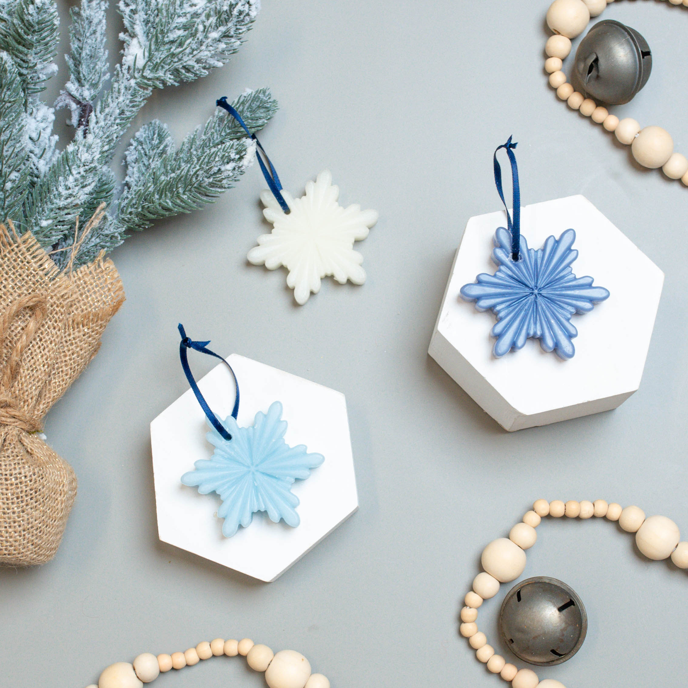 Three snowflake beeswax ornaments  in white, light blue, and dark blue surrounded by decorations.