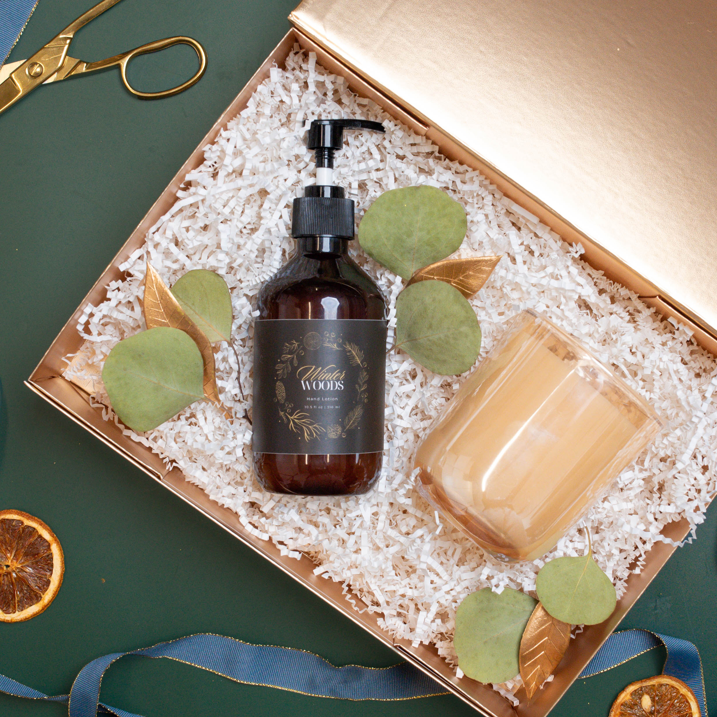 A bottle of hand lotion and a scented candle being packaged in a gold box.