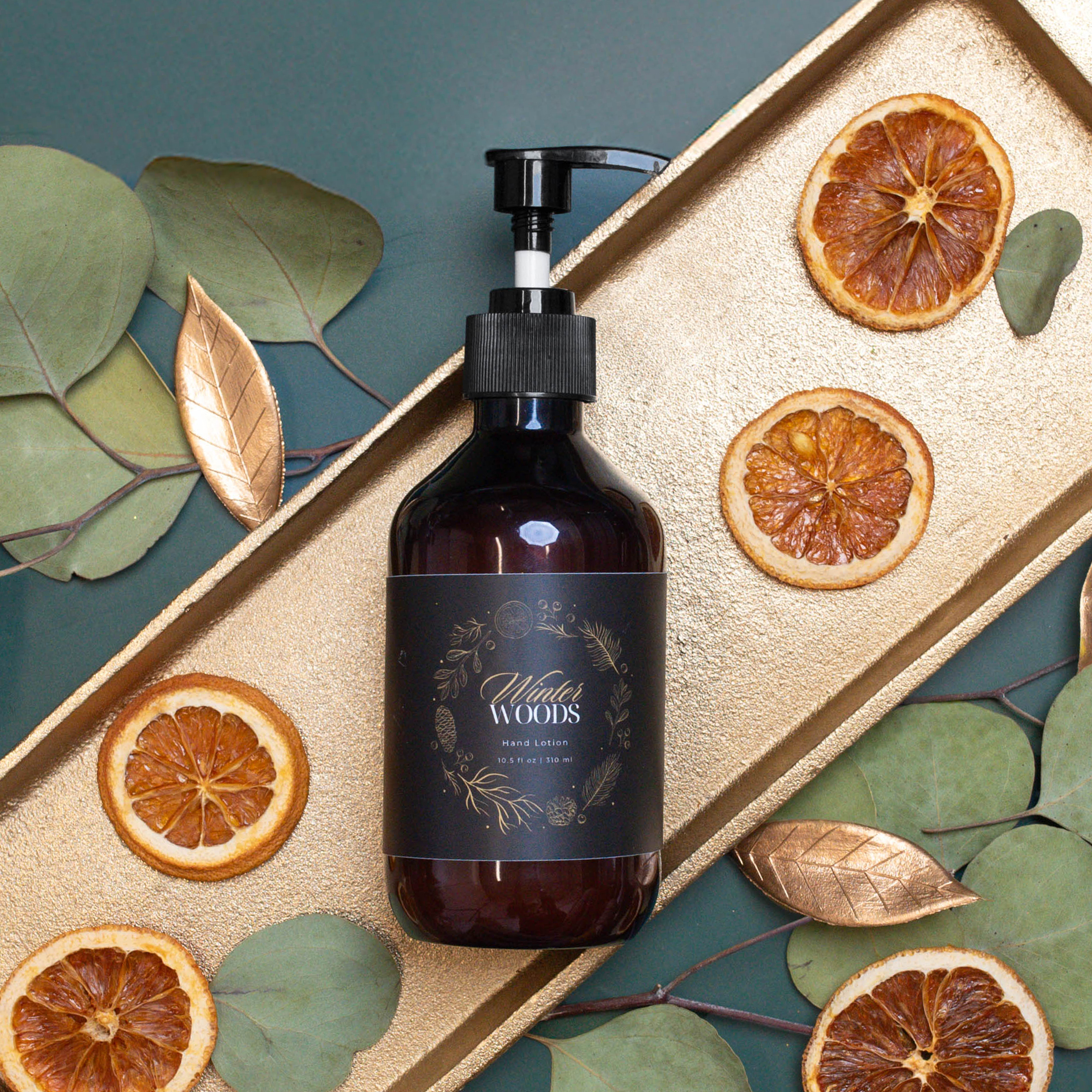 Hand lotion on a gold tray with eucalyptus and dried orange slices.