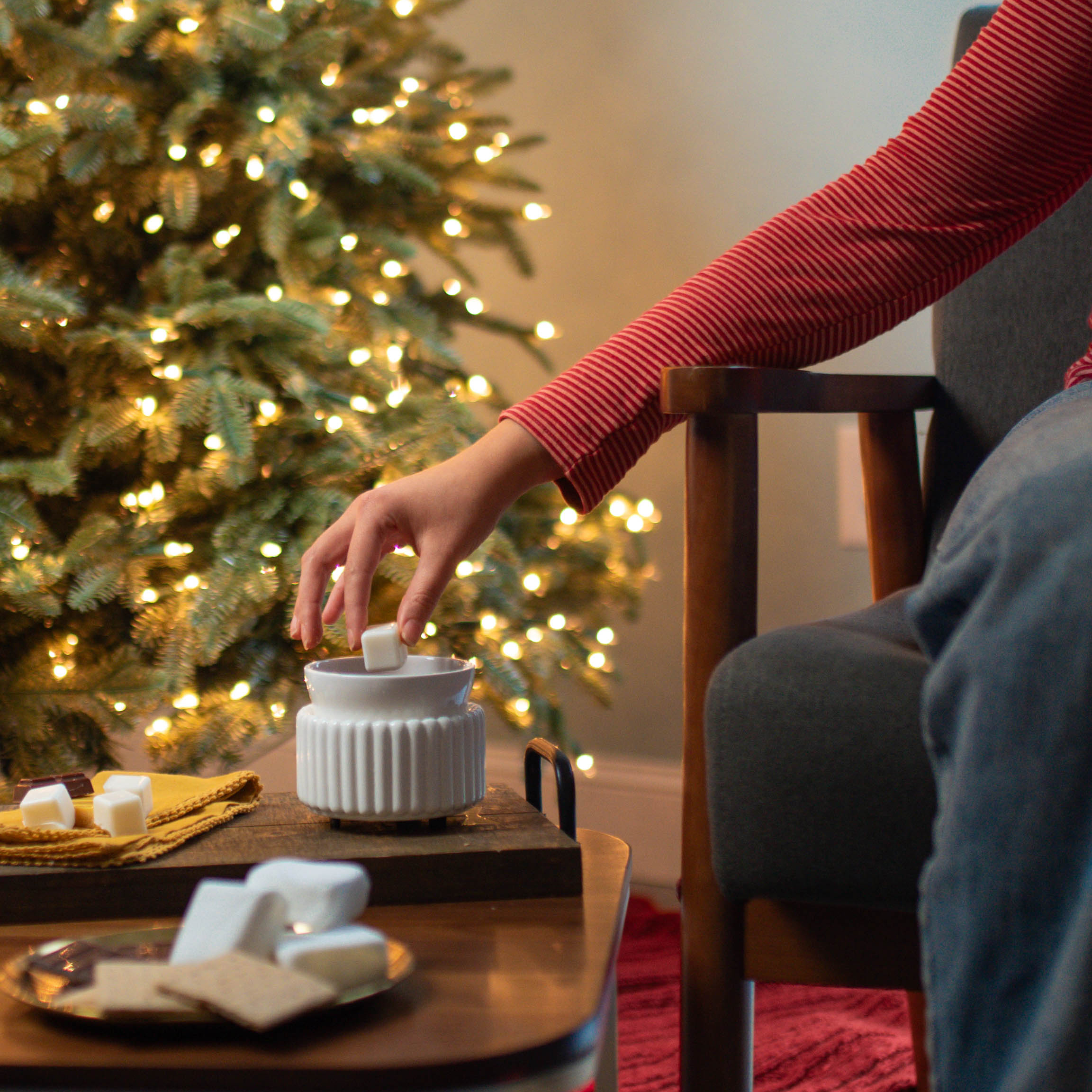 Person placing a wax melt into a warmer in front of a lit christmas tree.
