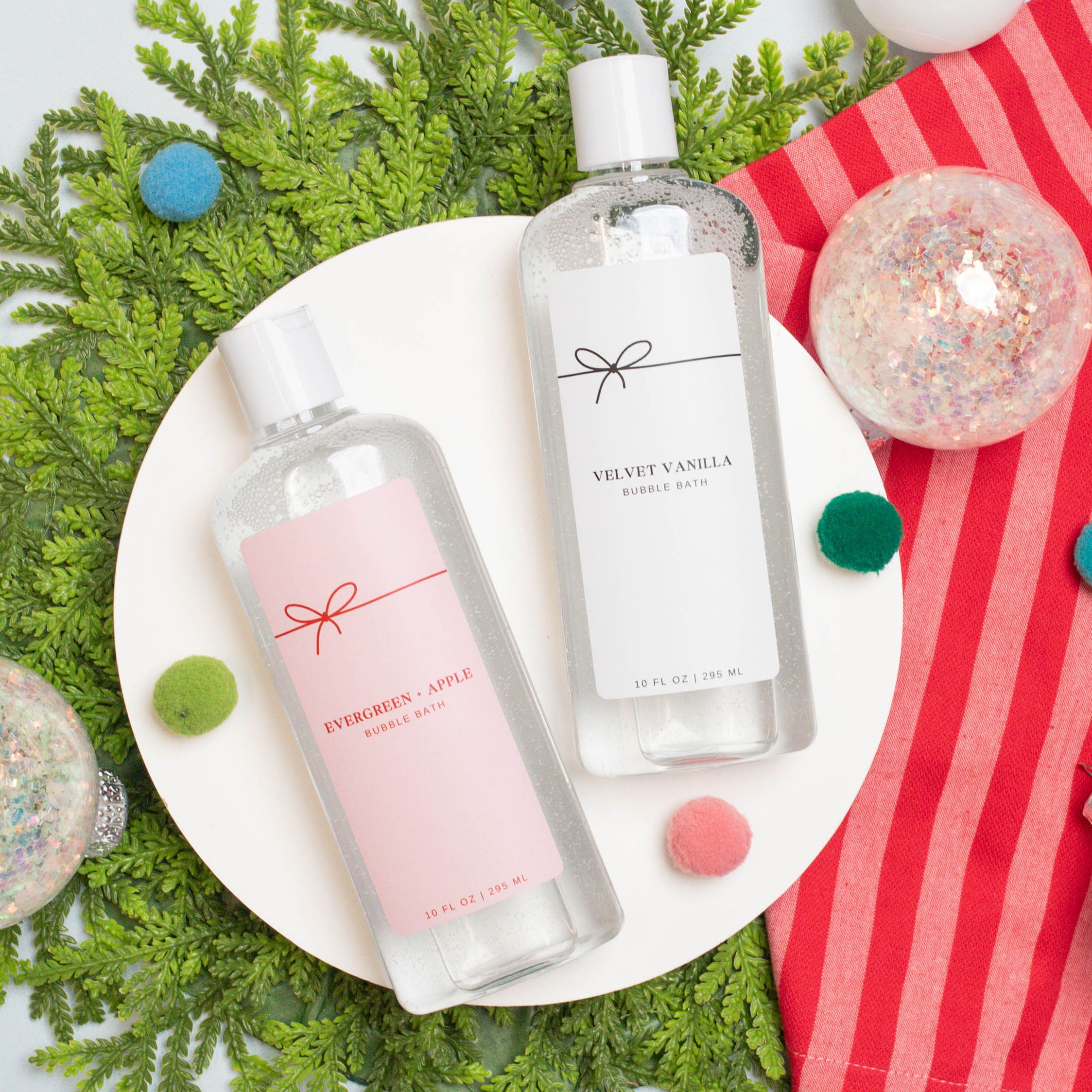 Top down view of two bottles of bubble bath with ornaments, greens, and a stripped towel. 