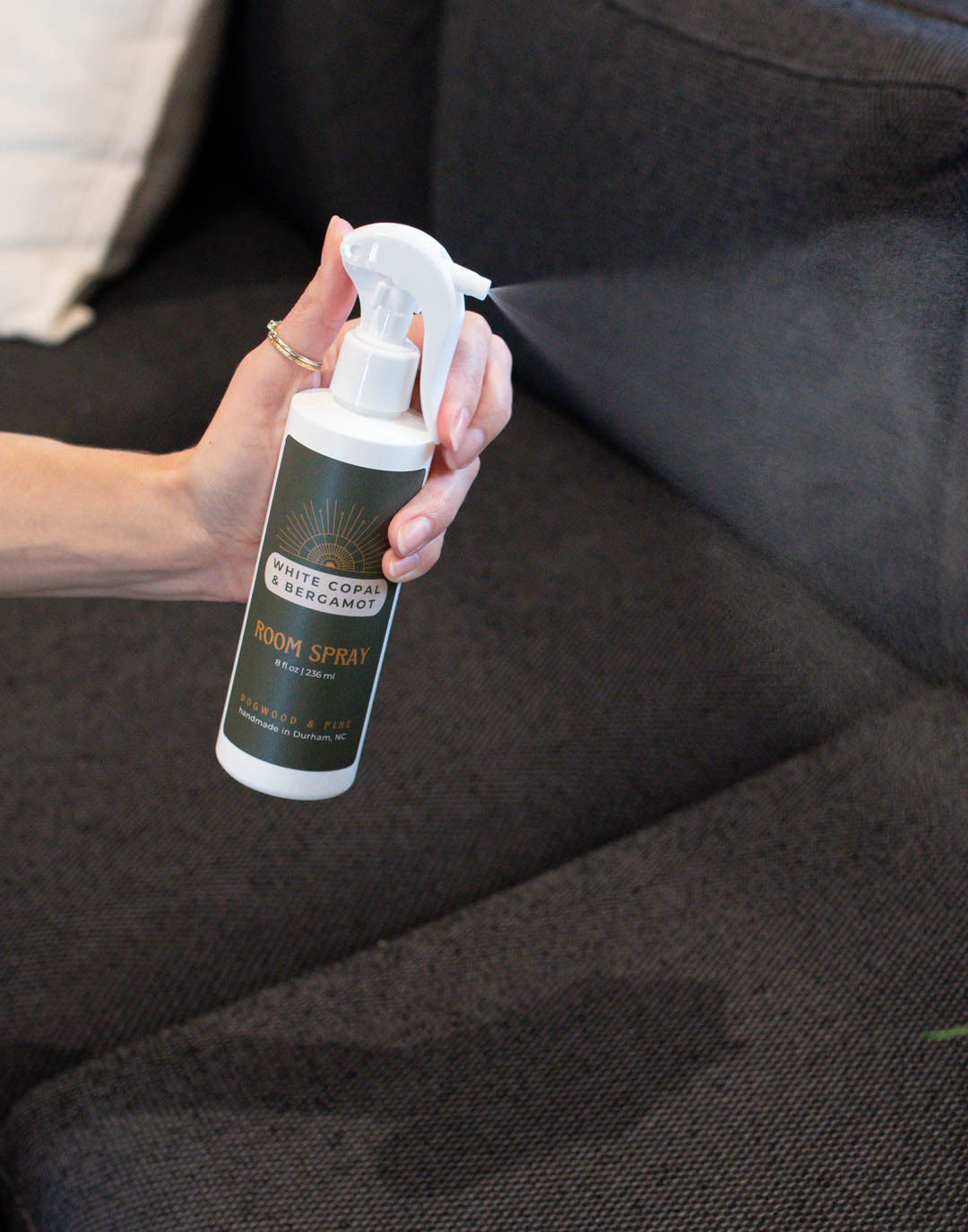 A light-skinned hand sprays a bottle of room spray made with CandleScience supplies