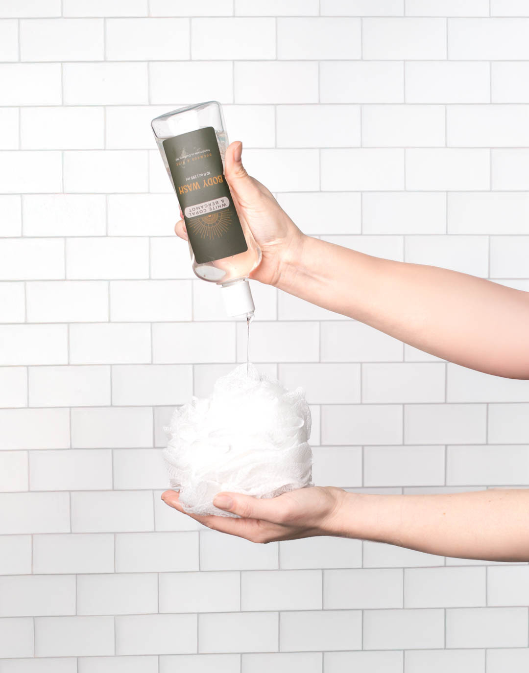 A light-skinned hand dispenses body wash made with CandleScience supplies on a shower poof