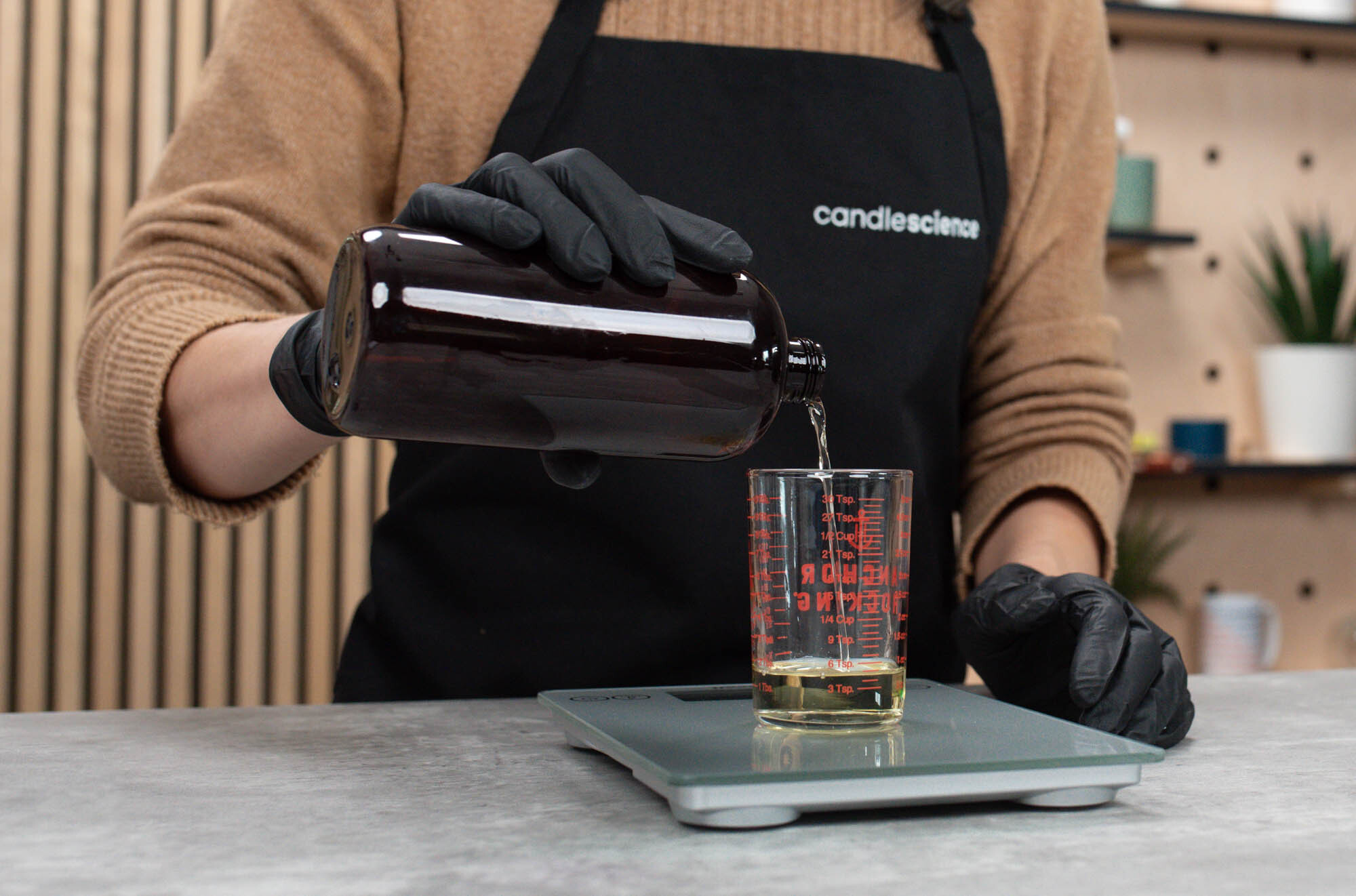 CandleScience fragrance oil being poured from a bottle into a beaker on a scale