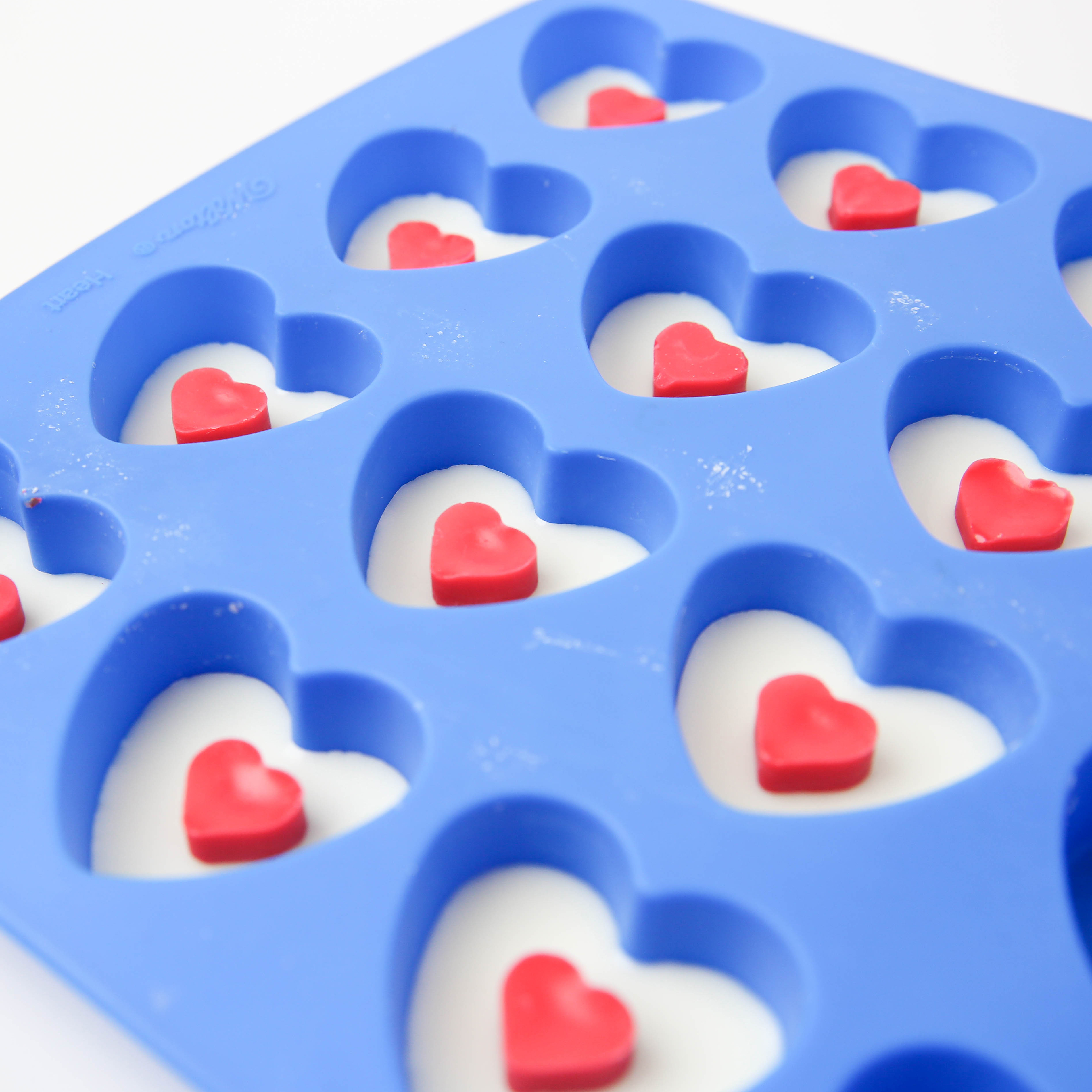 Small red heart wax melts placed in a heart mold half-filled with white wax