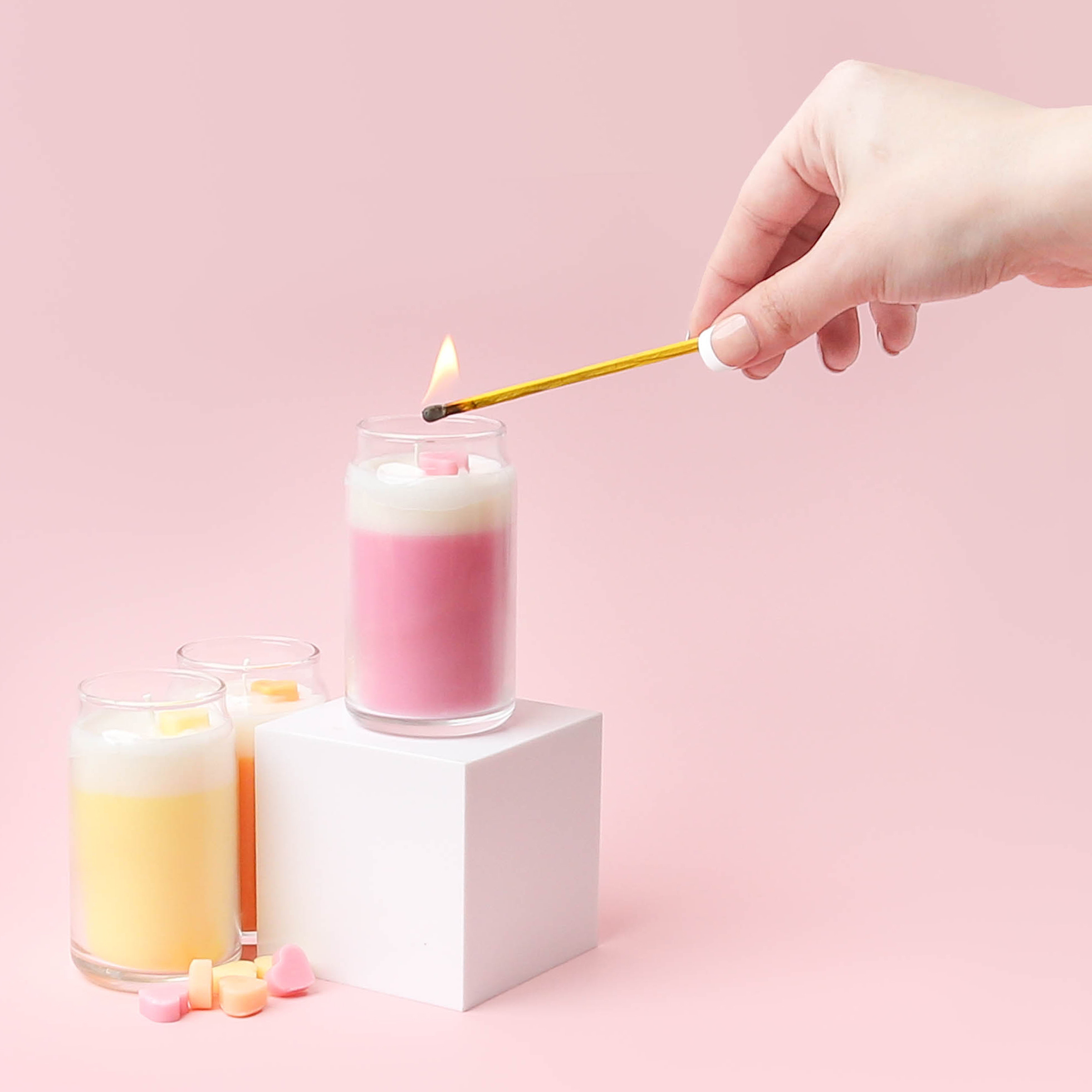 A hand lighting a pink mini candle with a match