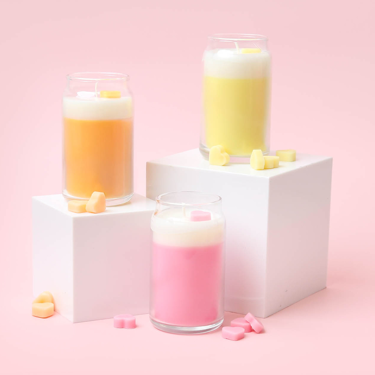 Three mini dessert themed candles with heart embeds in pink, yellow, and orange arranged on white boxes