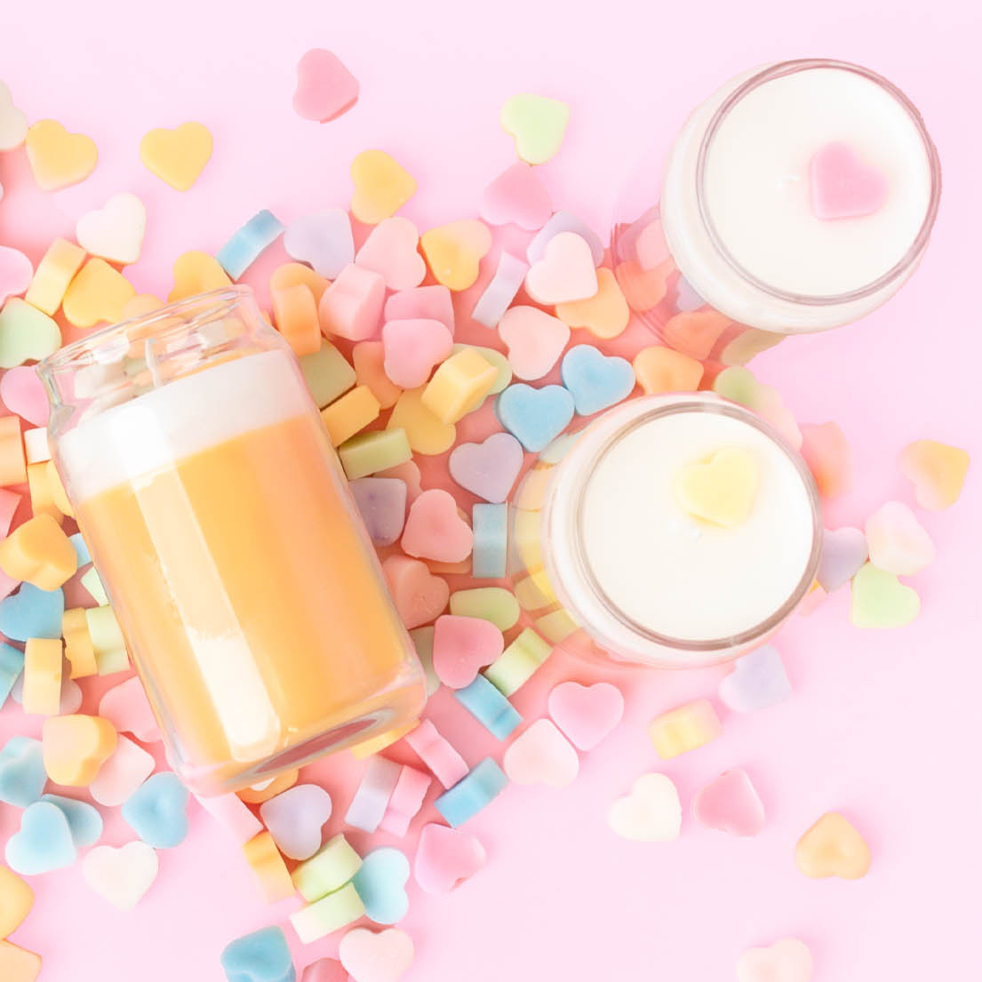 Three mini dessert themed candles with heart embeds on a pile of multi-colored candy heart wax melts