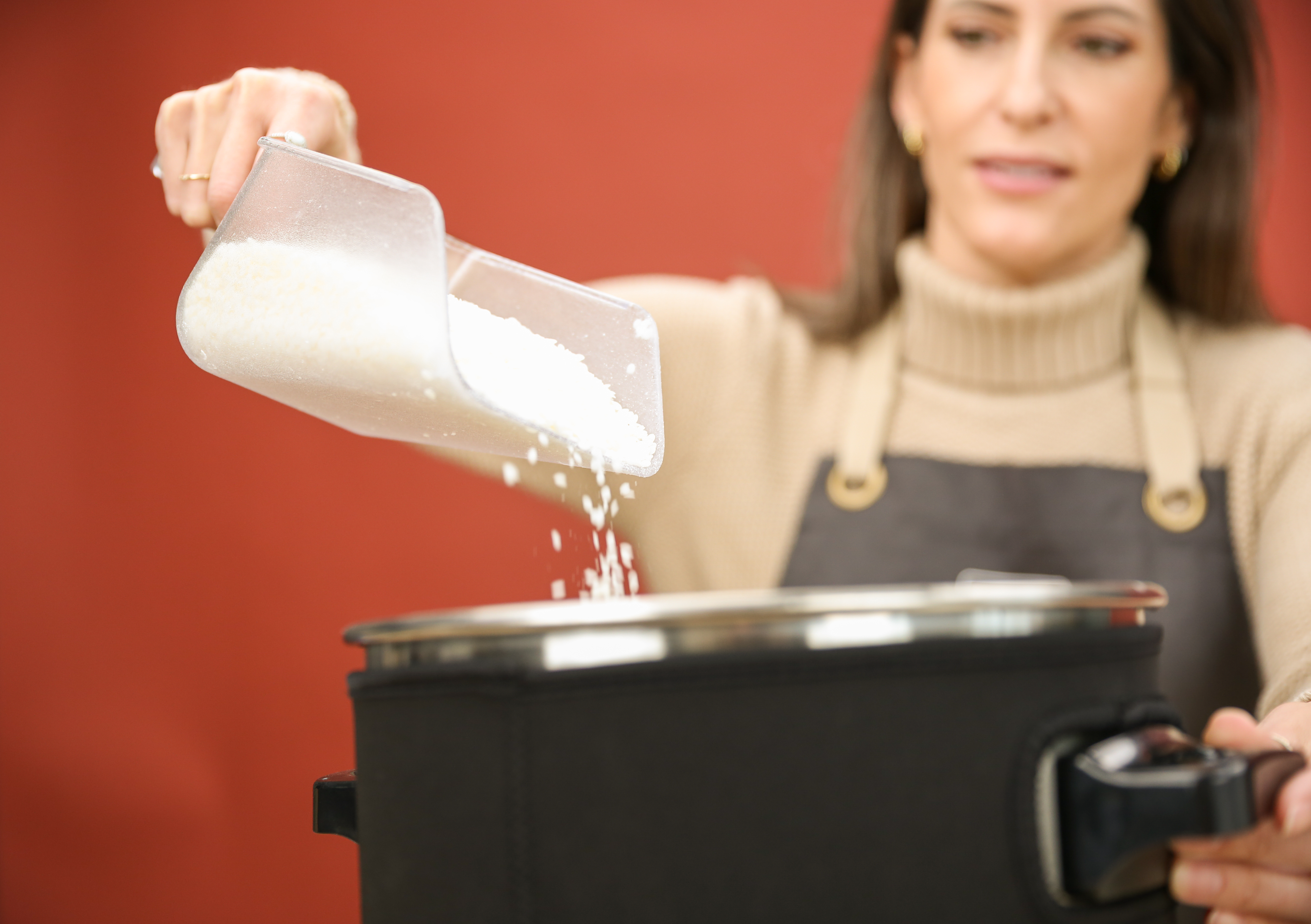 A light-skinned woman with brown hair pours wax flakes from a scoop into a wax melter