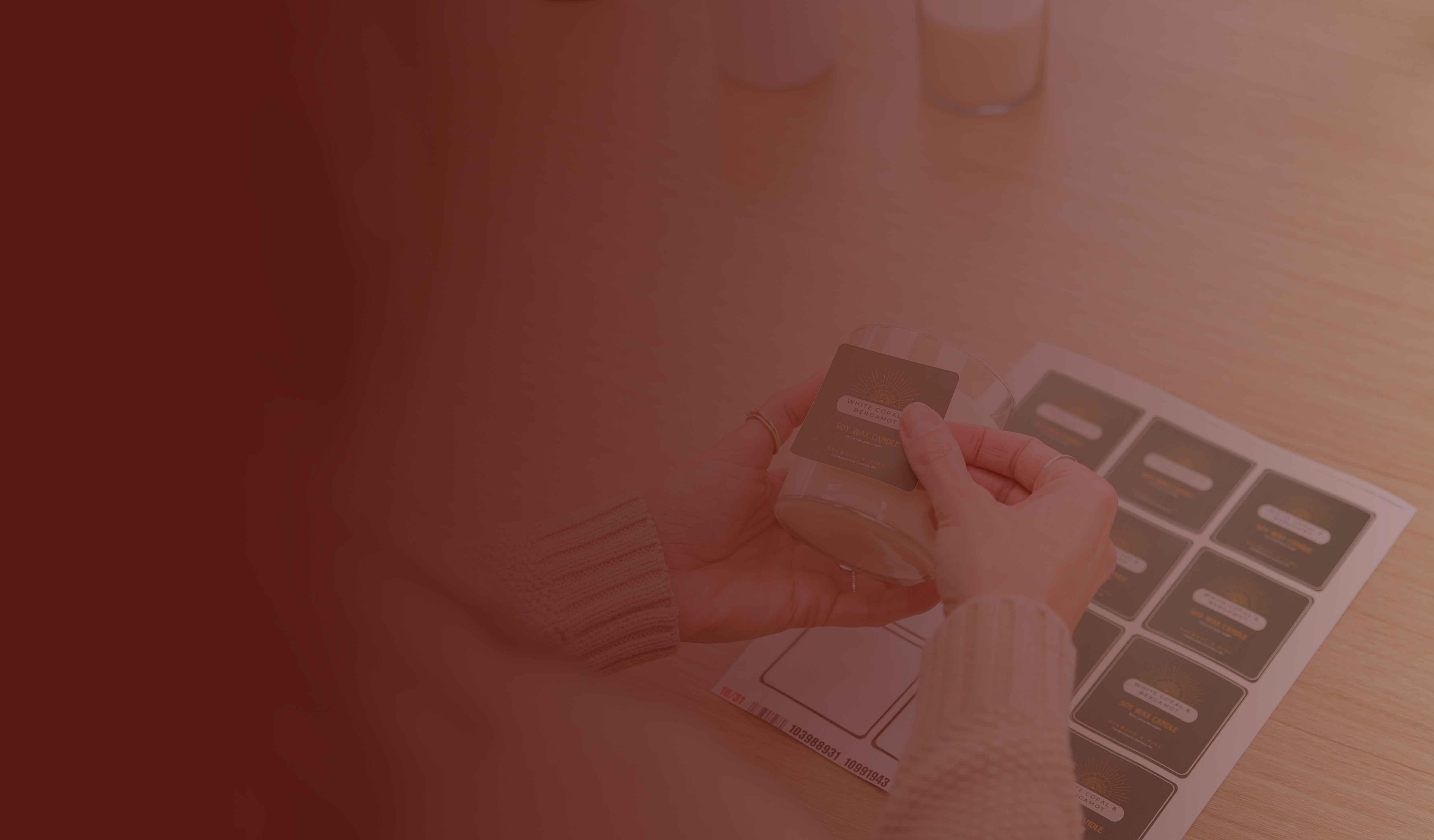 A pair of light-skinned hands places a candle label on a candle poured in a clear glass jar