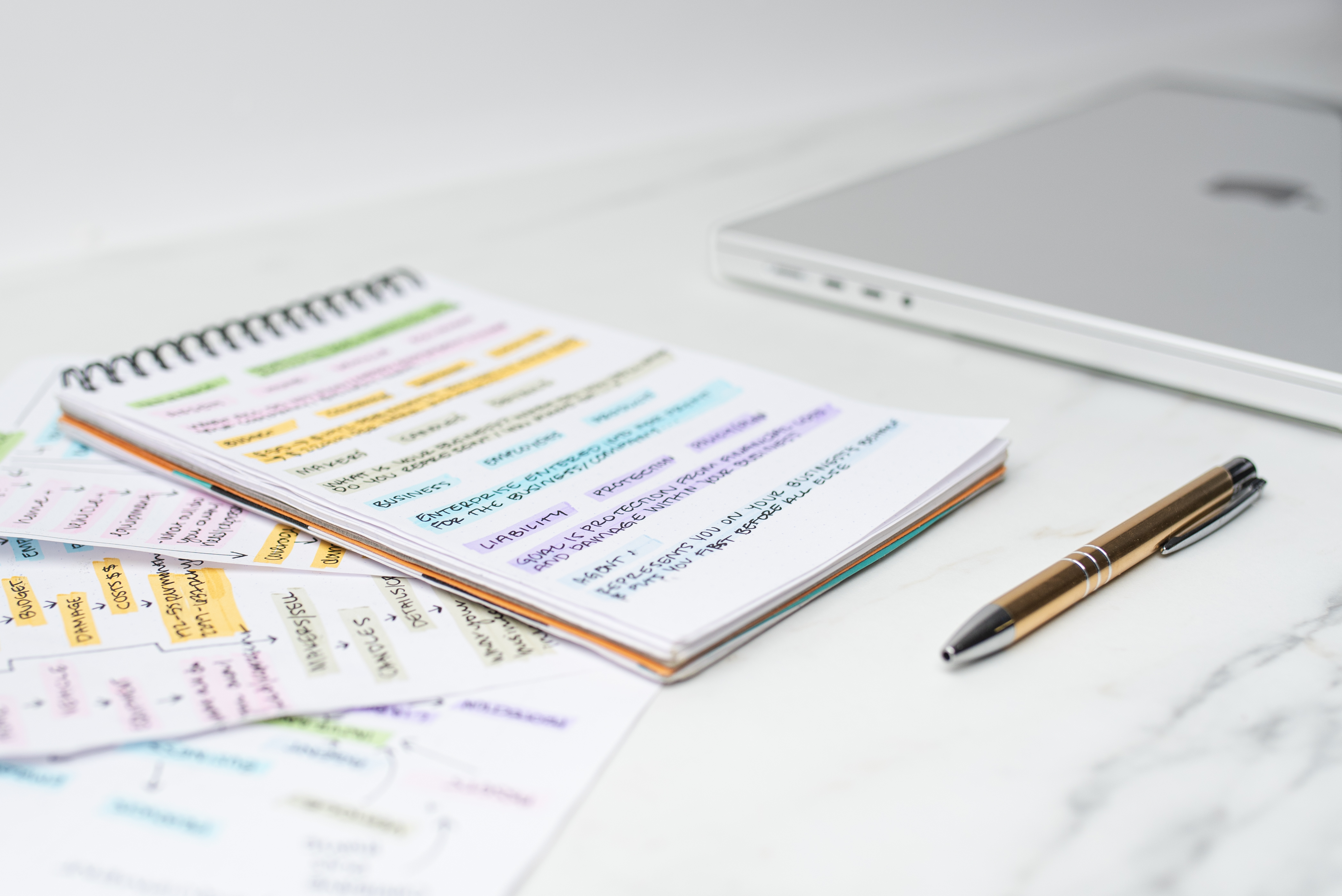 A pen and notepad with notes written on it lay next to a closed laptop