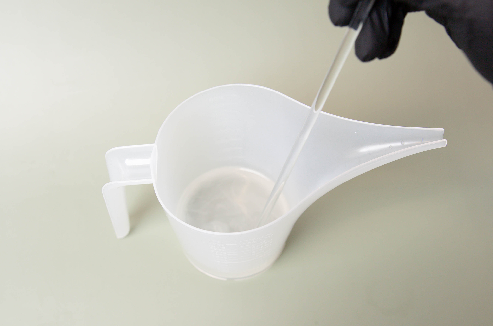 Stirring fine fragrance base and fine fragrance together in a funnel pouring pitcher.